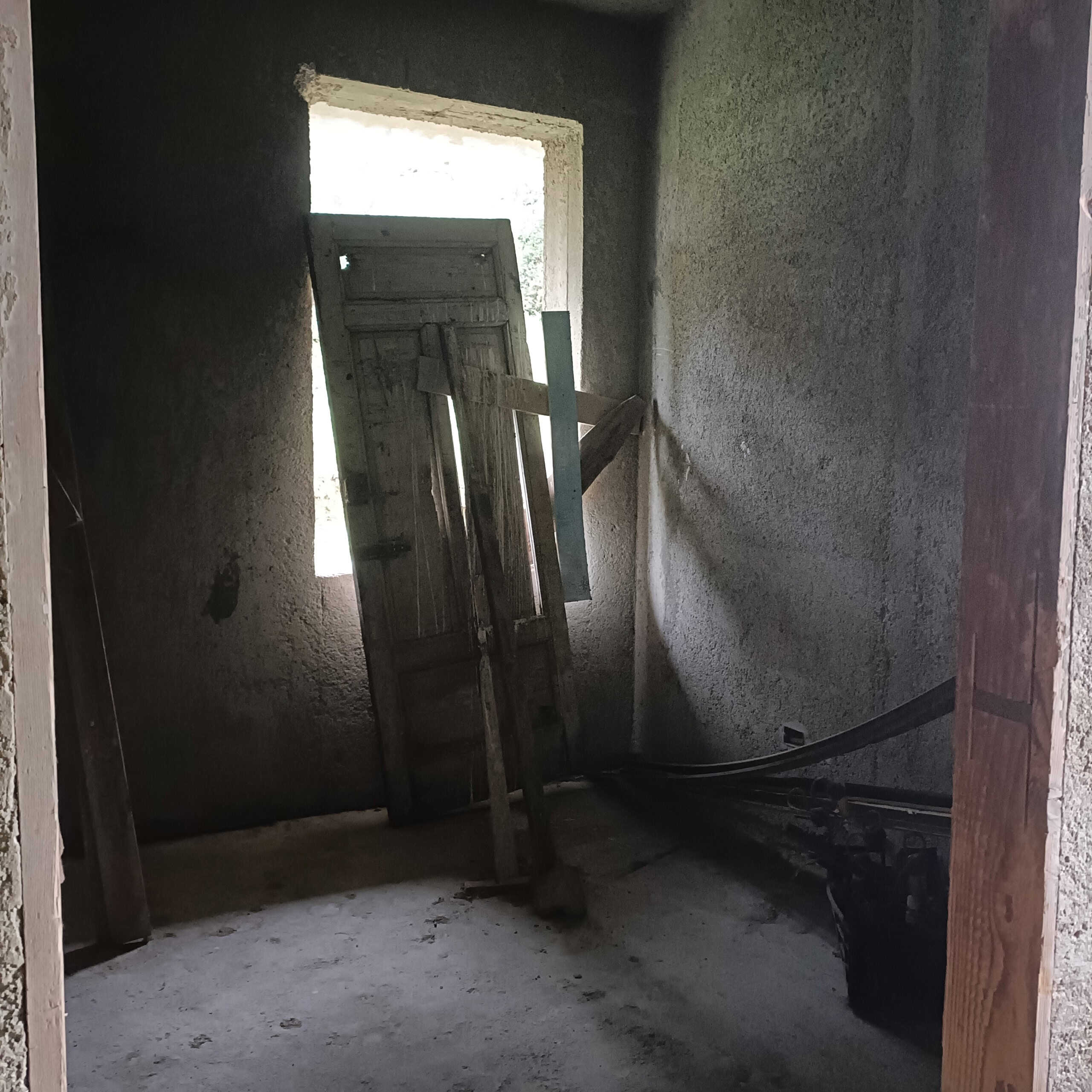 Porta finestra di una casa in costruzione con struttura di legno e pareti in cemento, luce naturale che entra dalla finestra, ambiente in fase di ristrutturazione, progetto edilizio NextCasa, edilizia e ristrutturazioni.