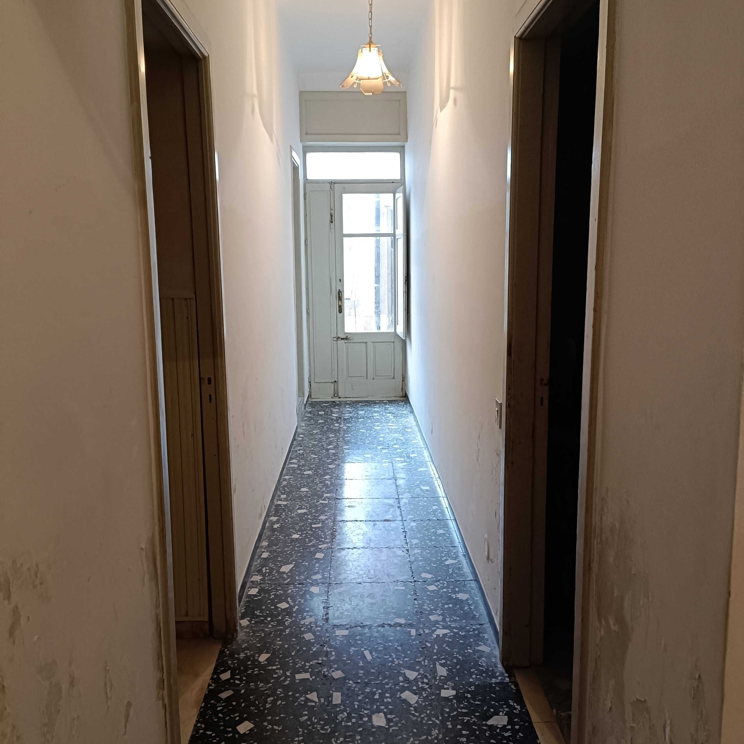 Corridor in appartamento con pavimento in terrazzo nero e pareti bianche, ingresso luminoso con porta finestra, stile classico e pratico, ideale per mutuo o vendita immobiliare.
