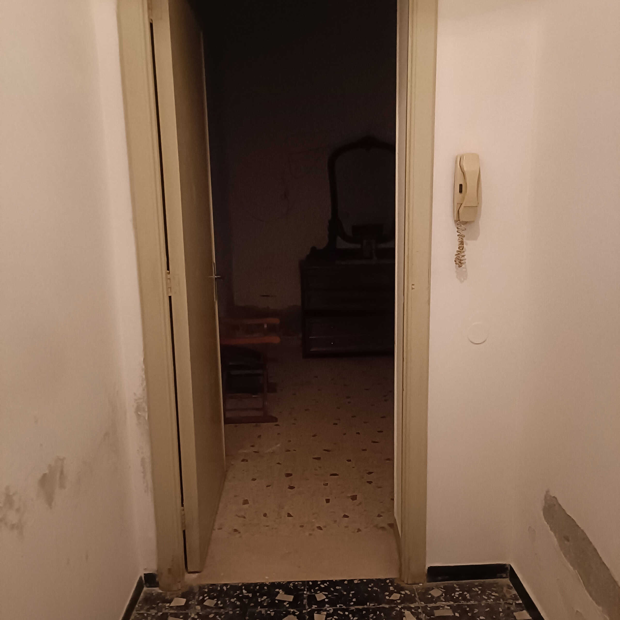 Deposito semi-interrato in un appartamento a NextCasa, zona con accesso tramite porta e pavimento in terrazzo colorato, pareti neutre, interfono e pareti leggermente usurate.