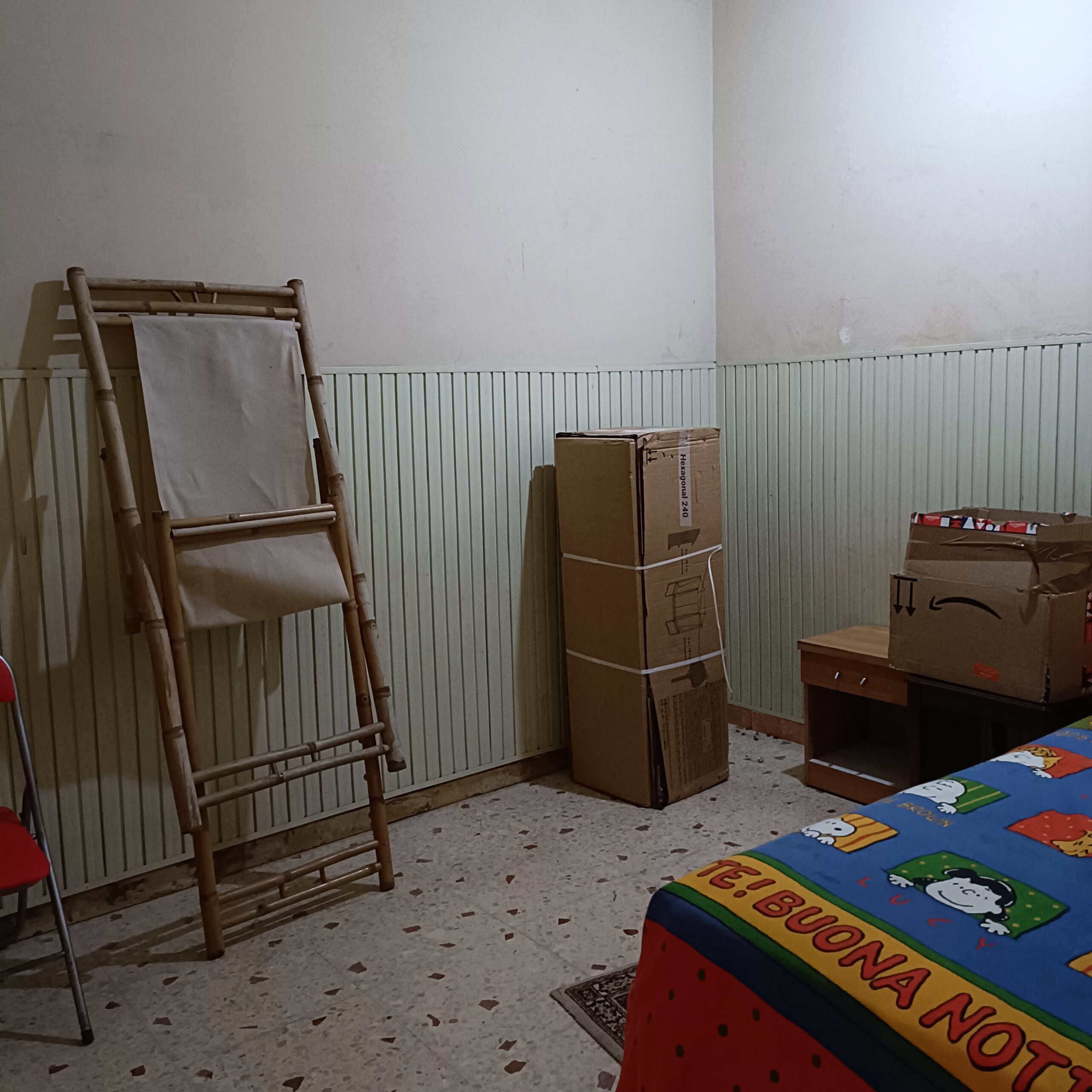 Scaffale in legno e tessuto in una stanza da letto con scatole di imballaggio e letto con copertura colorata decorativa divertente e natalizia.