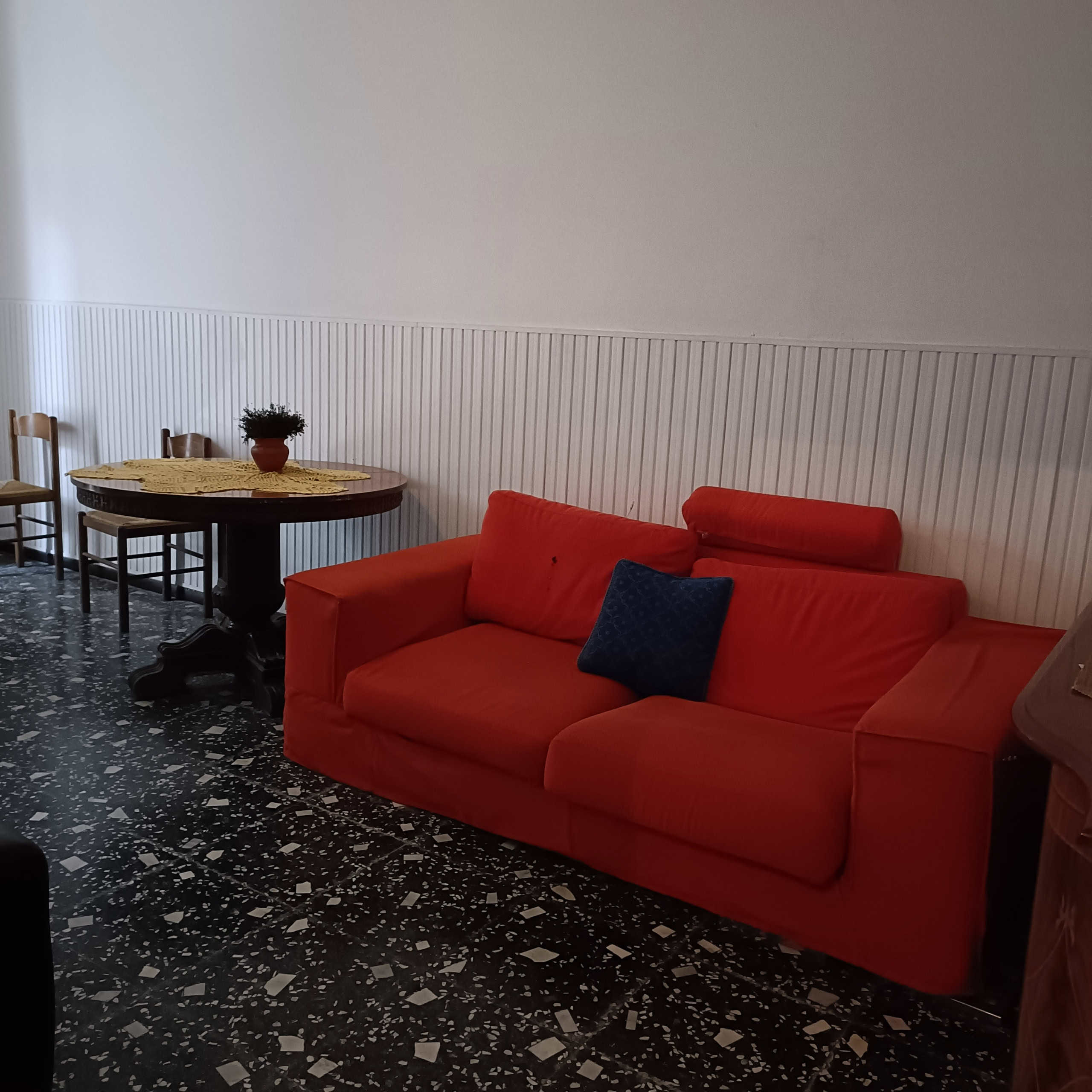 Divano rosso in soggiorno con parete a pannelli di legno bianca e pavimento in marmo nero con bianco, arredo accogliente e stile classico, ideale per appartamenti oggetto di intermediazione immobiliare NextCasa.