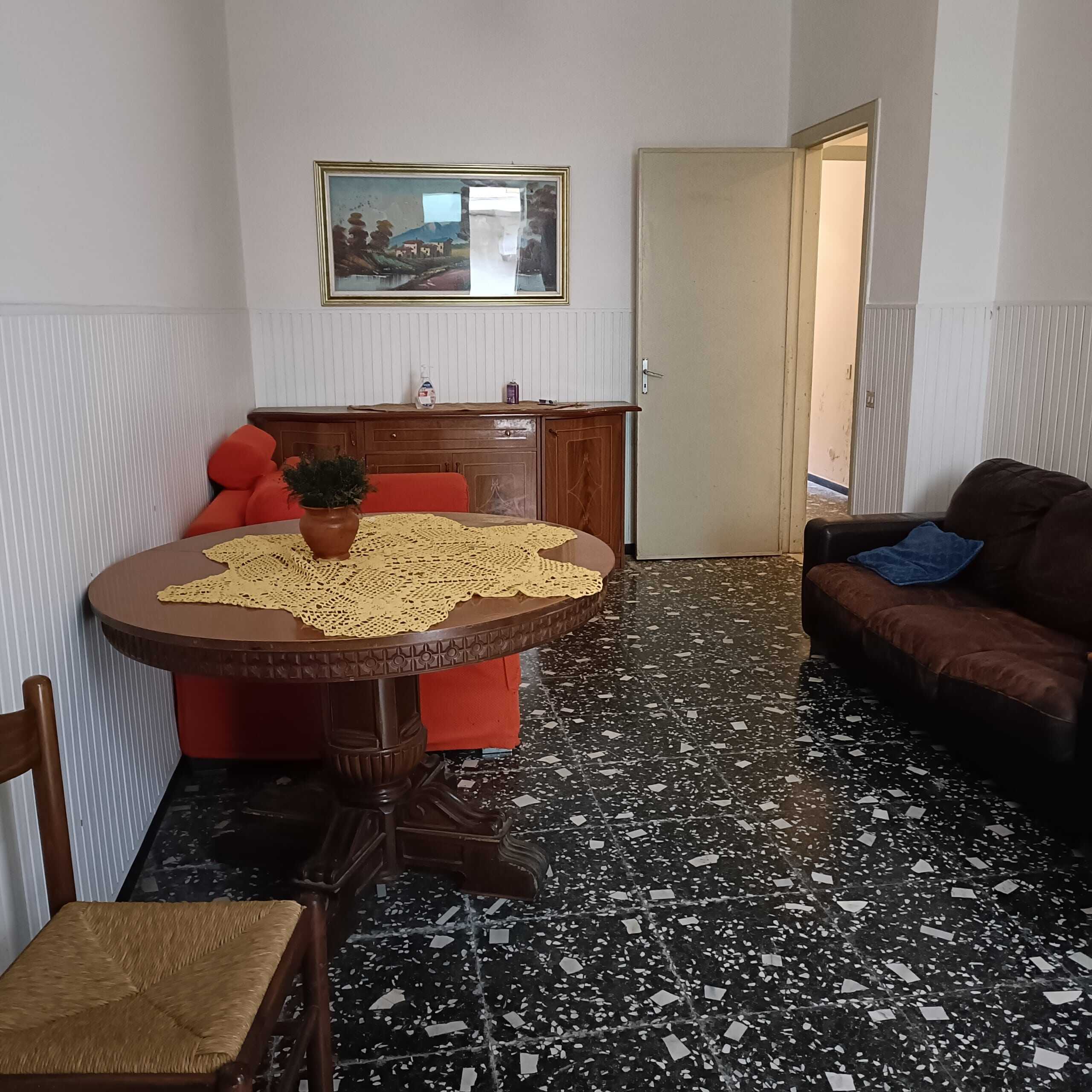 Poltrona rossa, soggiorno con tavolo rotondo, divano marrone, pareti rivestite in wengé, pavimento in pizzo di marmo nero e bianco, arredamento semplice, casa in vendita NextCasa, interno di abitazione classica italiana.