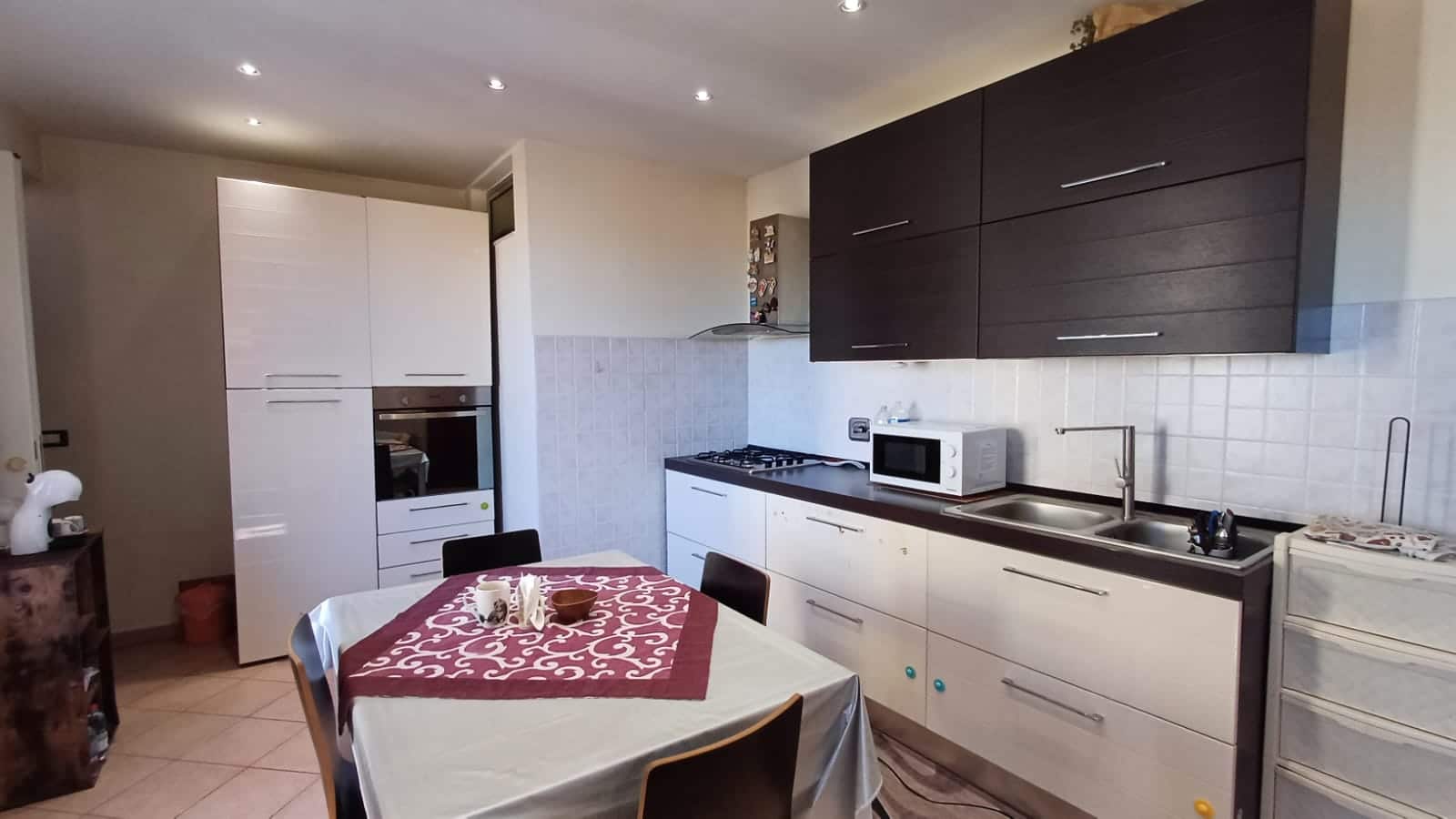 Lavanderia moderna con cucine compatte, elettrodomestici essenziali, pareti rivestite in ceramica bianca e mobili a parete in legno scuro, ideale per spazi abitativi pratici e funzionali.