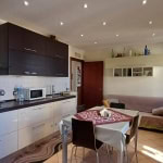 Spazio soggiorno e cucina in appartamento con arredi moderni, zona pranzo con tovaglia decorativa, area living con divano e accessori, ideale per immobili e affitti residenziali NextCasa.
