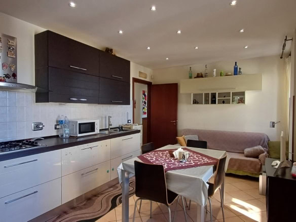 Spazio soggiorno e cucina in appartamento con arredi moderni, zona pranzo con tovaglia decorativa, area living con divano e accessori, ideale per immobili e affitti residenziali NextCasa.