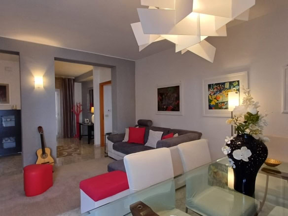 Ampio soggiorno moderno con arredi eleganti e pareti decorate con opere d'arte, ambiente luminoso con illuminazione soffusa e vaso di fiori freschi, ideale per valorizzare gli spazi residenziali di NextCasa.