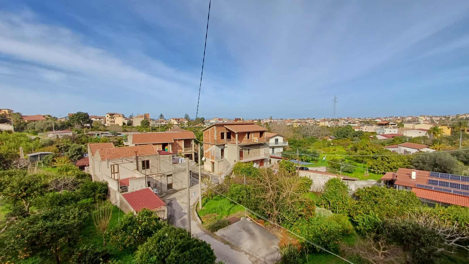 Viste panoramiche di case e case unifamiliari in un quartiere residenziale con vegetazione verde e tetti con pannelli solari, rappresentando un ambiente abitativo tranquillo e sostenibile.