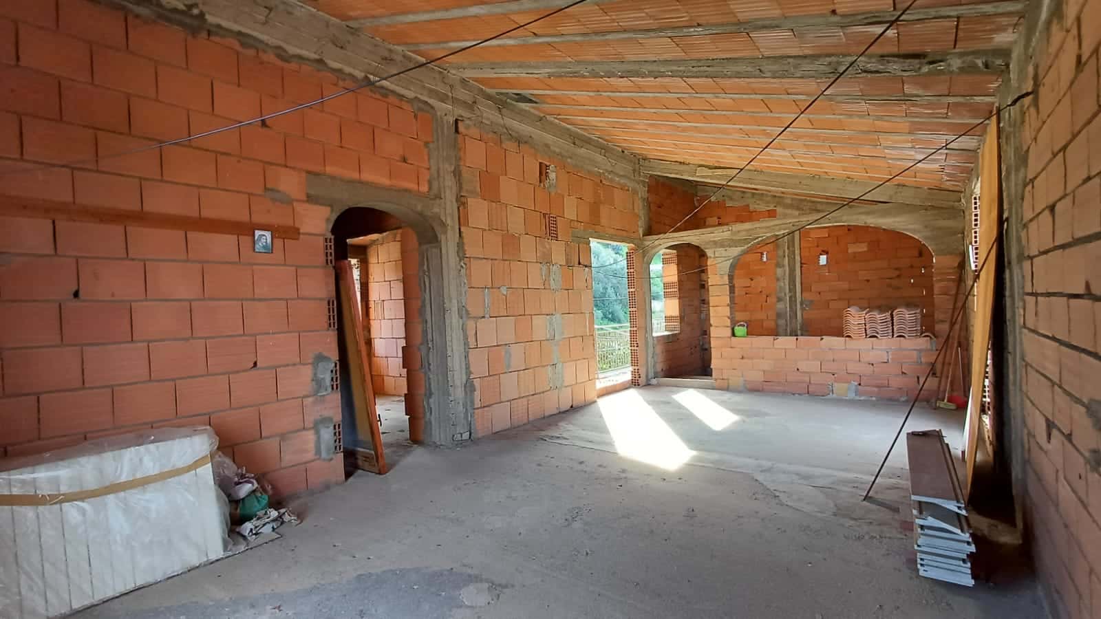 Cerchi un'immagine di interni di una casa in costruzione con pareti di mattoni rossi e archi in cemento, ideale per il settore edilizio e immobiliare.