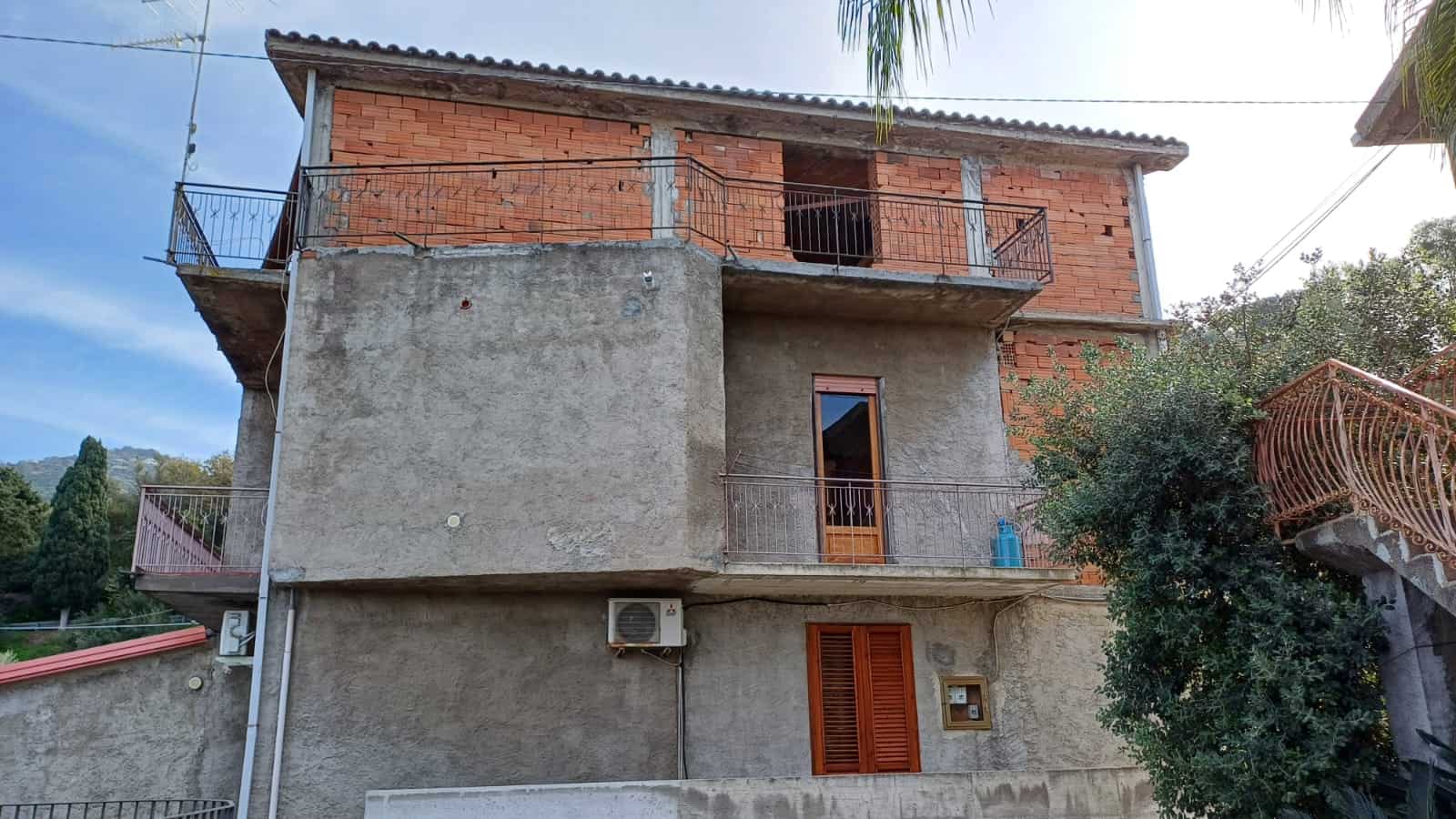 Casa in costruzione con struttura in mattoni e cemento, balconi in ferro battuto e ambiente naturale circostante, soluzione abitativa ideale in zona tranquilla e panoramica.