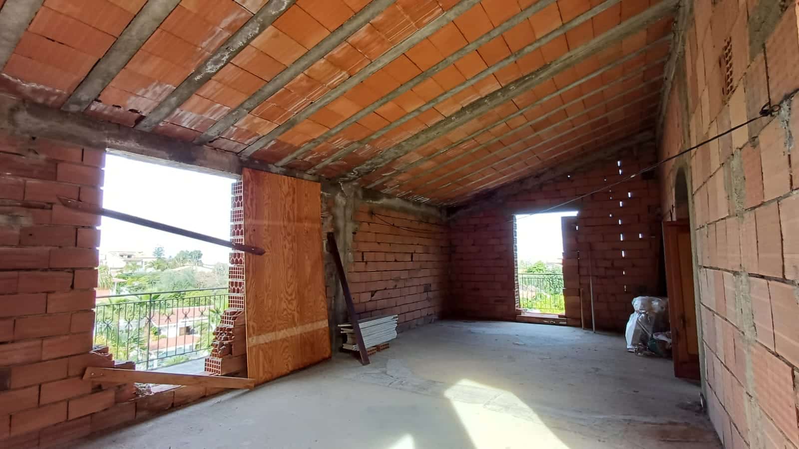 Tetto in costruzione con mattoni e cemento, apertura su terrazza, interno di una casa in fase di edilizia dotata di balcone e vista panoramica.