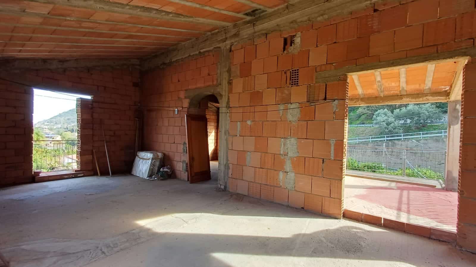 Vecchia casa in costruzione con pareti in mattoni rossi e grandi finestre aperte, vista sulla campagna, progetto di ristrutturazione edilizia, interni ancora da completare.
