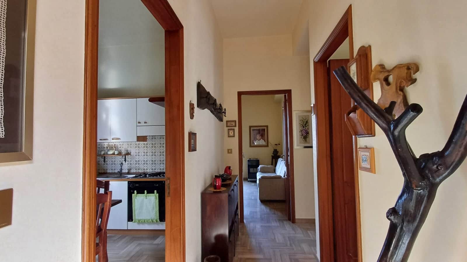 Ampia vista dell'ingresso di una casa con mobili in legno e decorazioni rustiche, collegamenti tra cucina, soggiorno e corridoio, atmosfera accogliente e tradizionale.