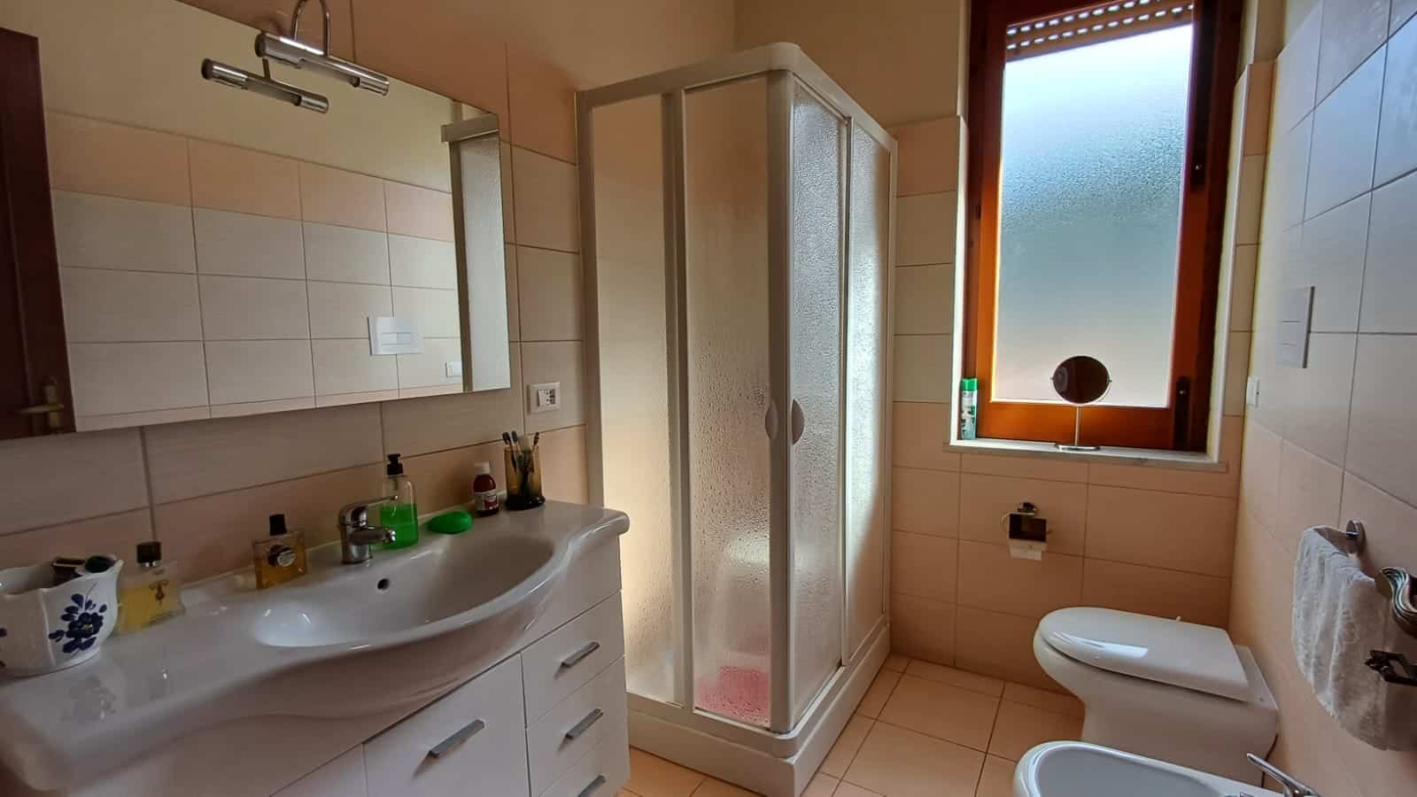 Lavabo moderno con specchio LED, doccia in cristallo e finestra con vetro opacizzato, bagno in stile semplice e funzionale, ideale per case in vendita o affitto.