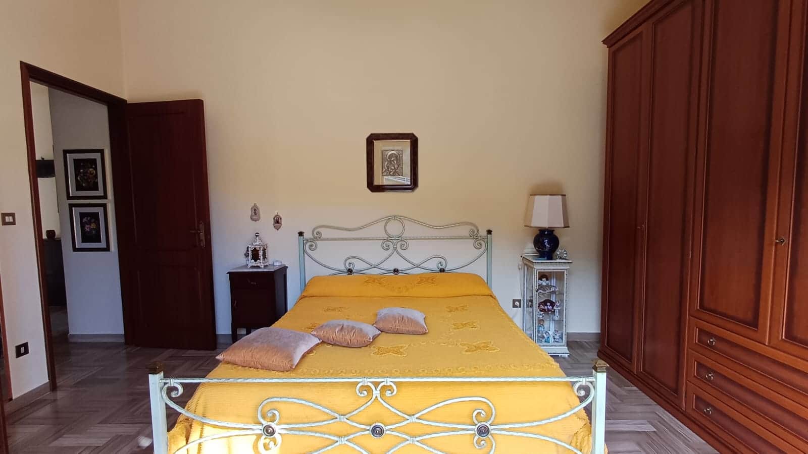 Letto matrimoniale in camera da letto con biancheria gialla, mobili in legno e armadio grande, decorazioni tradizionali, atmosfera accogliente, ideale per case in stile classico o rustico.