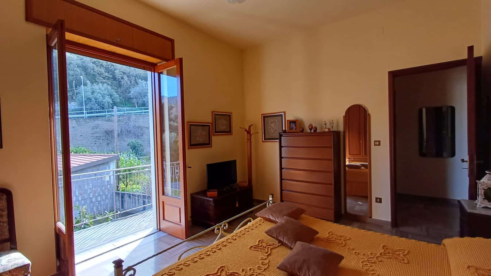 Balcone con vista panoramica sulla natura e arredamento accogliente di una camera da letto in stile classico con mobili in legno, pareti di colore caldo e grandi finestre che illuminano l'ambiente.