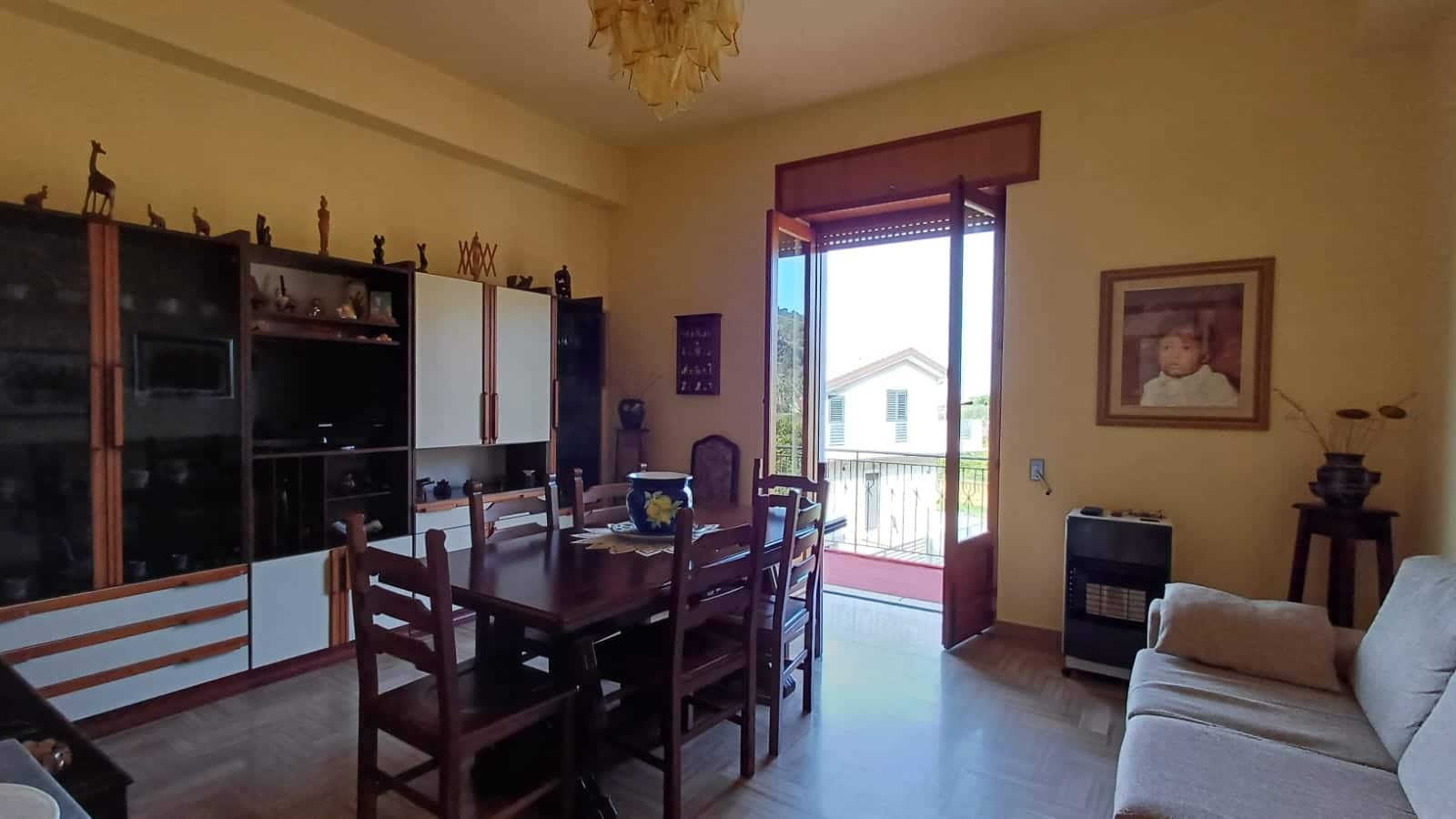 Soggiorno accogliente in stile classico con mobili in legno, pareti gialle, camino, e accessori decorativi. Ampio spazio con tavolo da pranzo e balcone con vista sulla natura, ideale per vivere in comfort.
