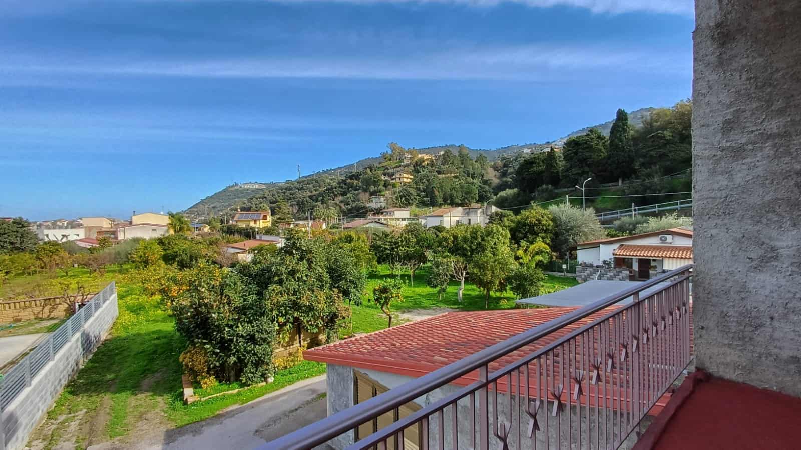 Arredamento casa vista panoramica montagna e natura in campagna, con balcone in primo piano, case, alberi e cime montuose sullo sfondo, perfetto per realizzare immobili esterni e proprietà rurali.