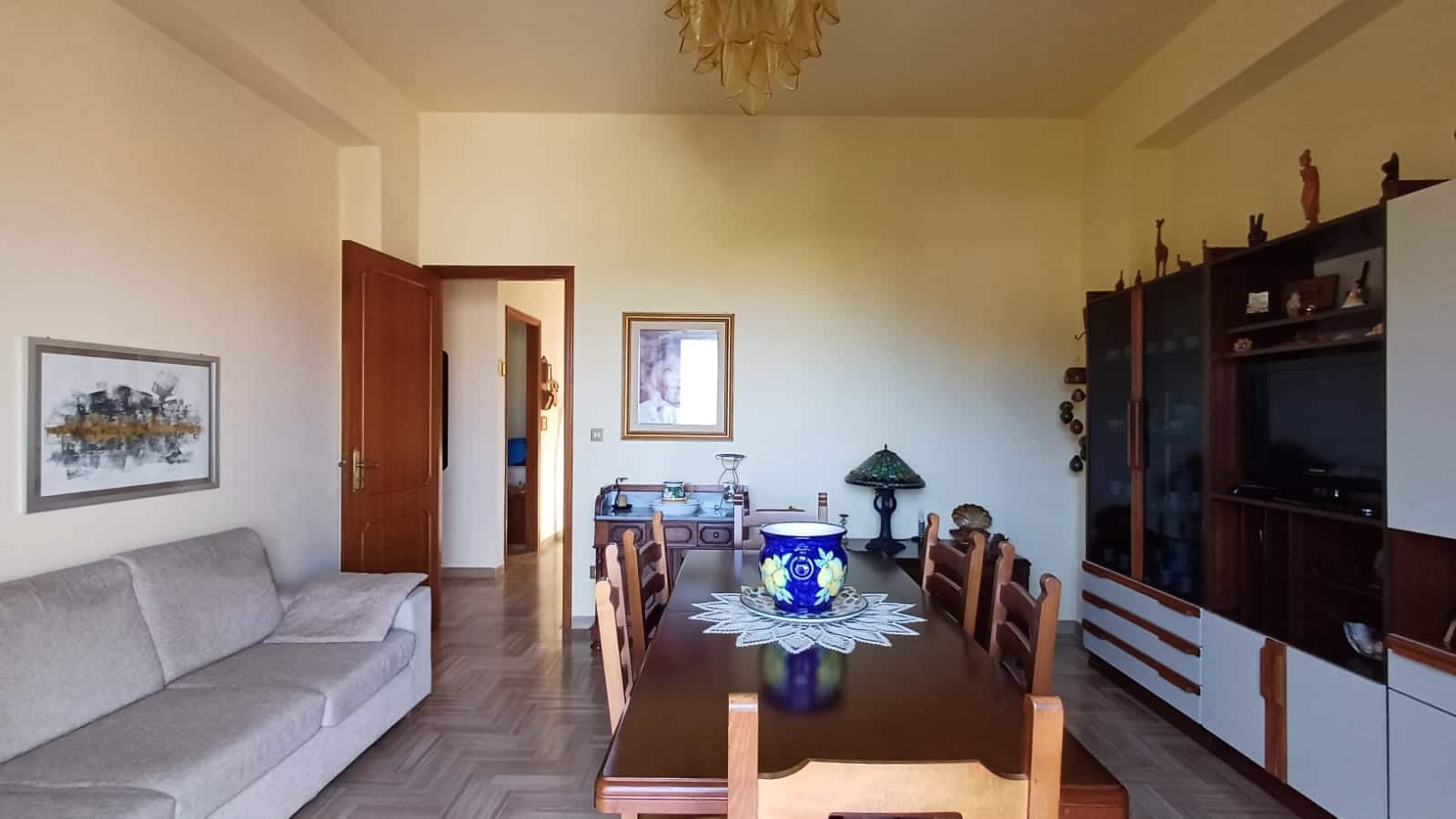 Soggiorno spazioso con divano, tavolo in legno e arredi classici, decorazioni eleganti, ambiente luminoso e accogliente, ideale per abitazione privata o investimento immobiliare.