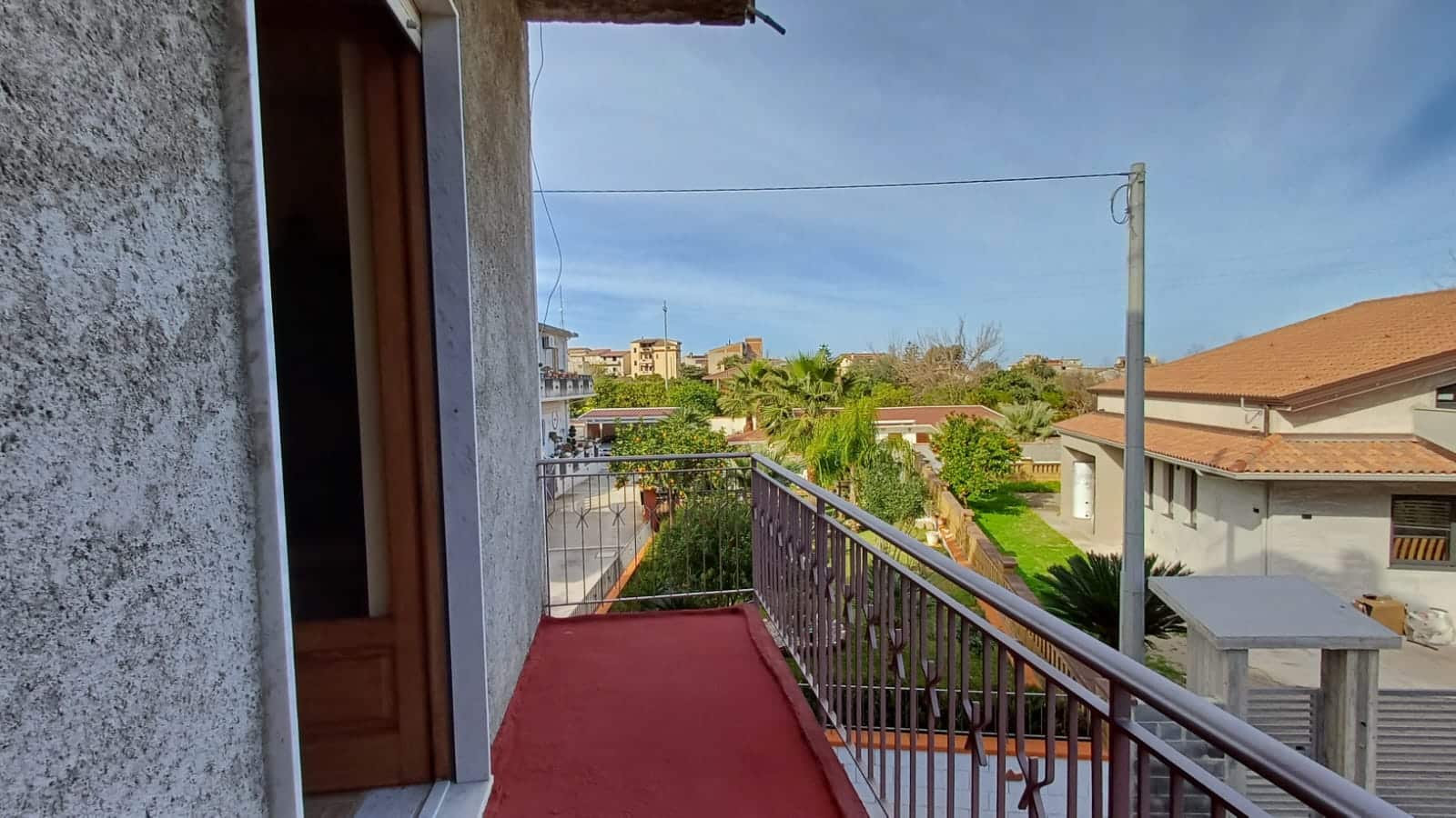 Balcone con vista su quartiere residenziale, case con tetti rossi, alberi e cielo sereno, ideale per vivere in tranquillità e godersi l'ambiente urbano e naturale della zona.