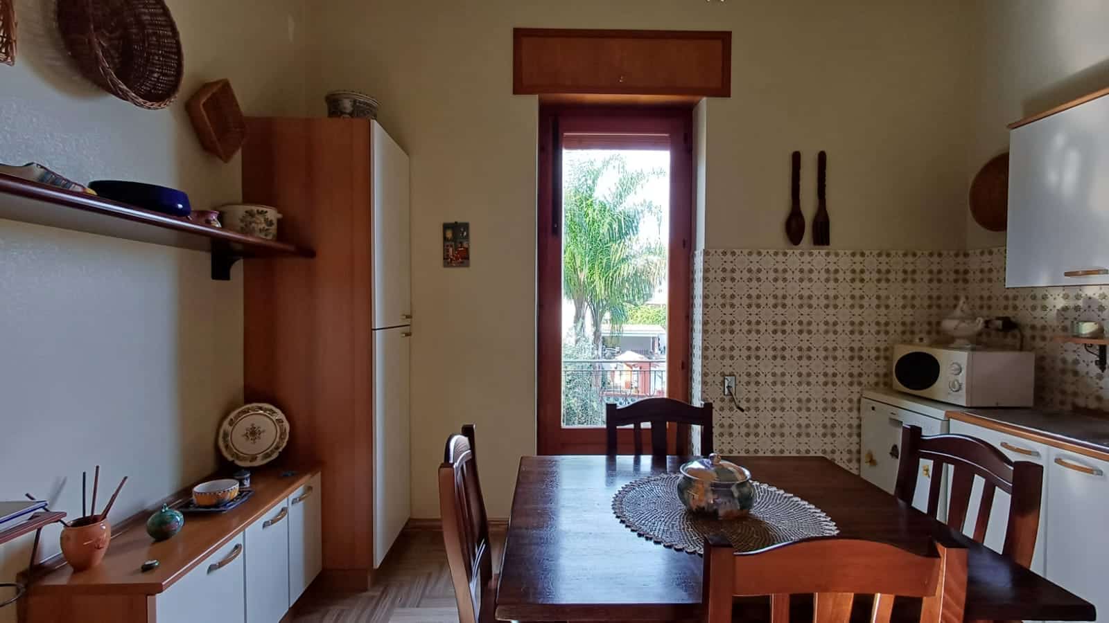 Finestra con vista sul giardino in cucina, arredamento rustico, tavolo in legno con tovaglietta, cucina funzionale con microonde e accessori in stile tradizionale italiano.