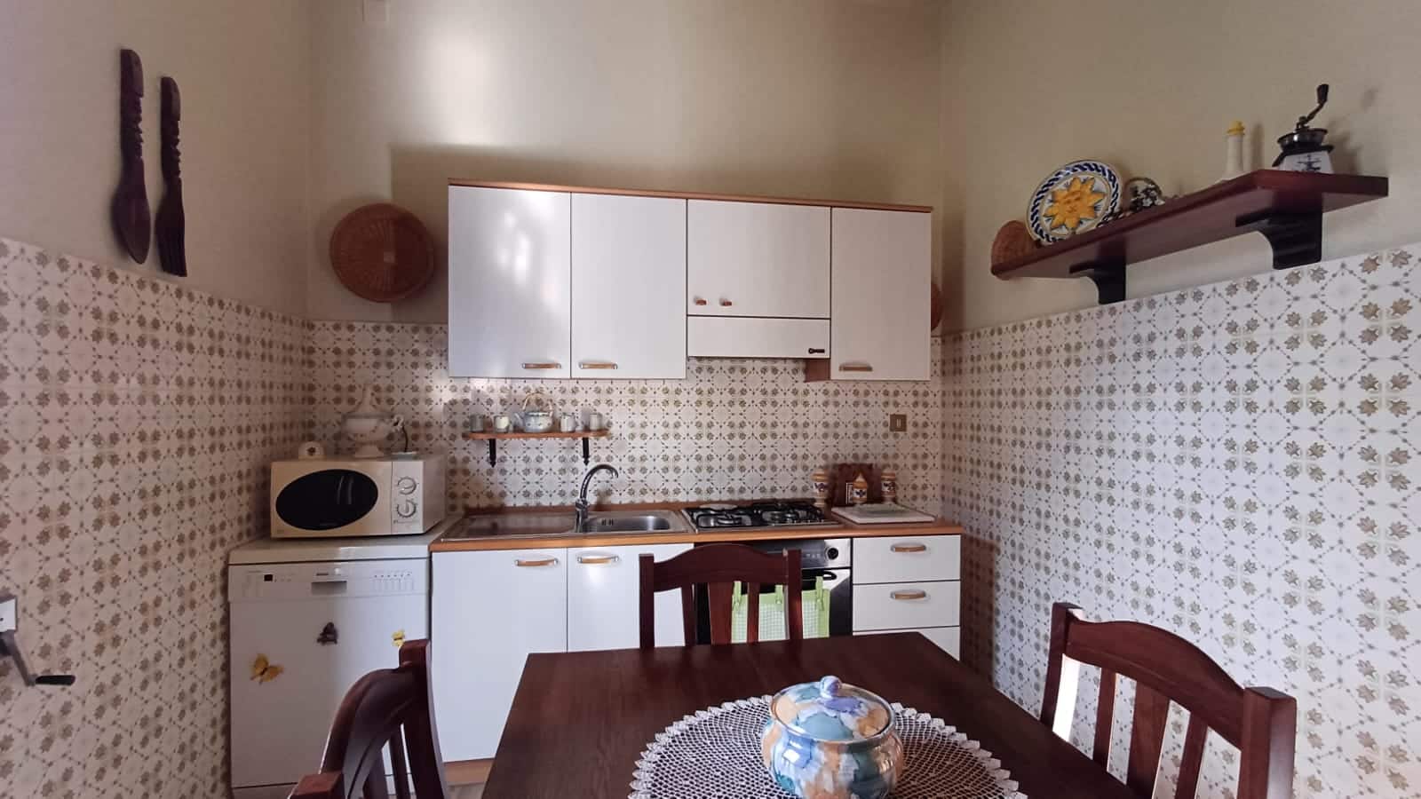 Cucina abitabile con mobili bianchi, pareti decorate con ceramiche vintage, tavolo in legno e accessori da cucina rustici, corazza cucina in stile classico e accogliente.