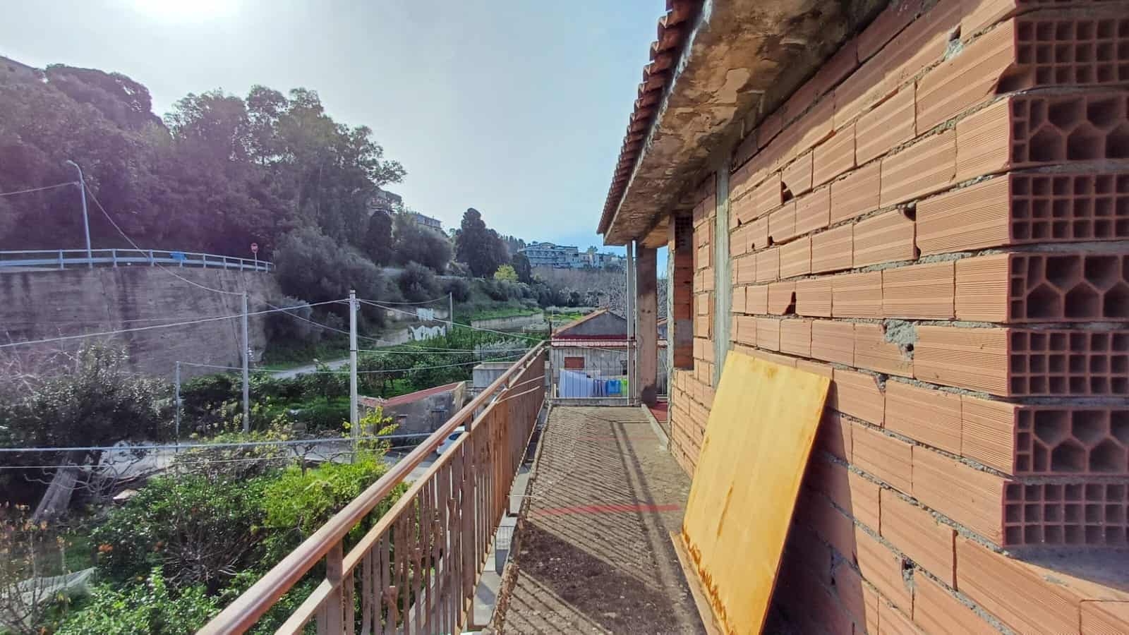 Balcone di un edificio in fase di costruzione con vista su un paesaggio verde e collinare, muri in mattoni e struttura ancora incompleta, in un contesto residenziale di montagna.