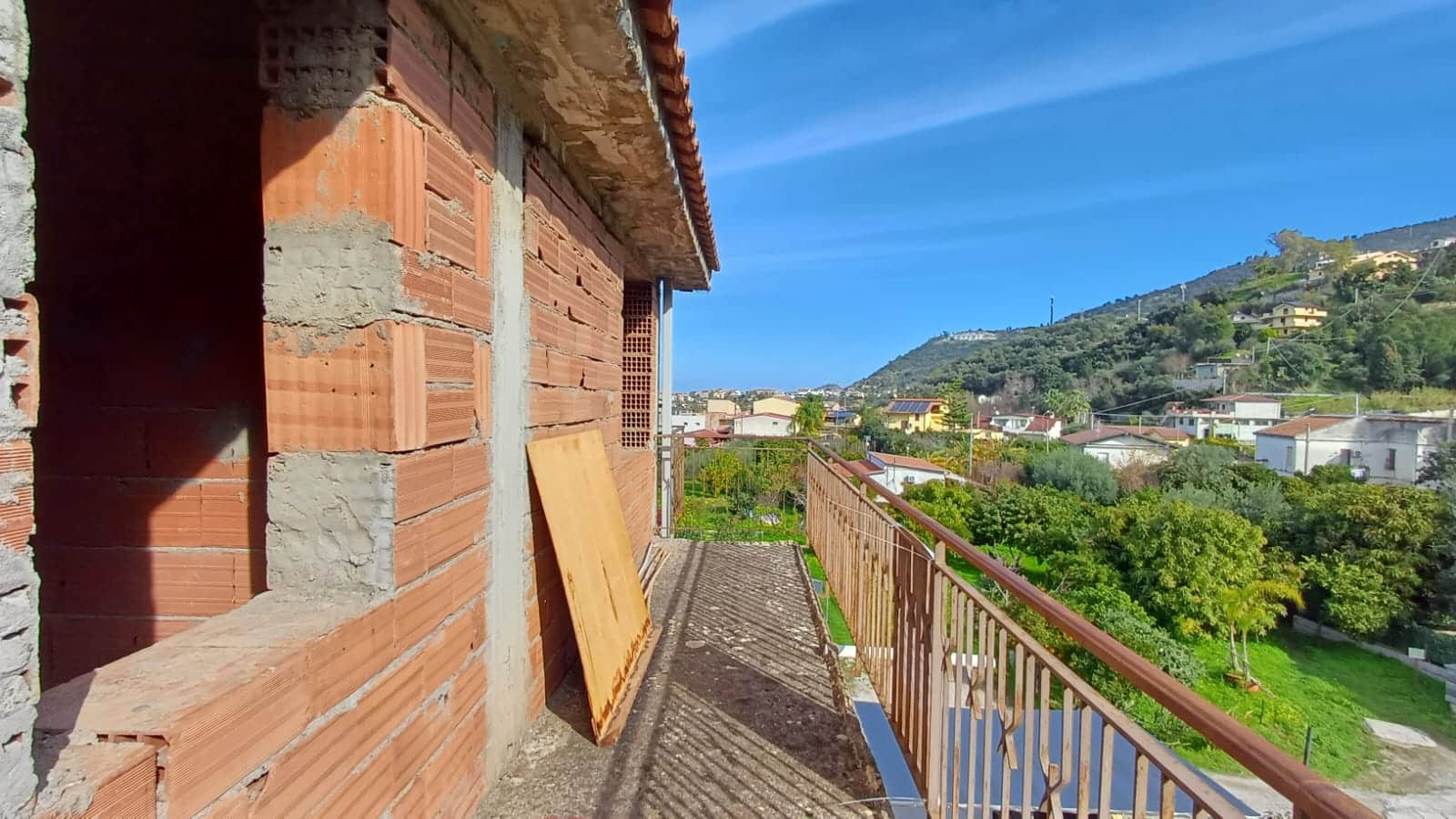 Scorcio di balcone di un edificio in costruzione con vista panoramica su case e natura in collina, ambienti residenziali, progetto immobiliare NextCasa, nuove opportunità abitative.