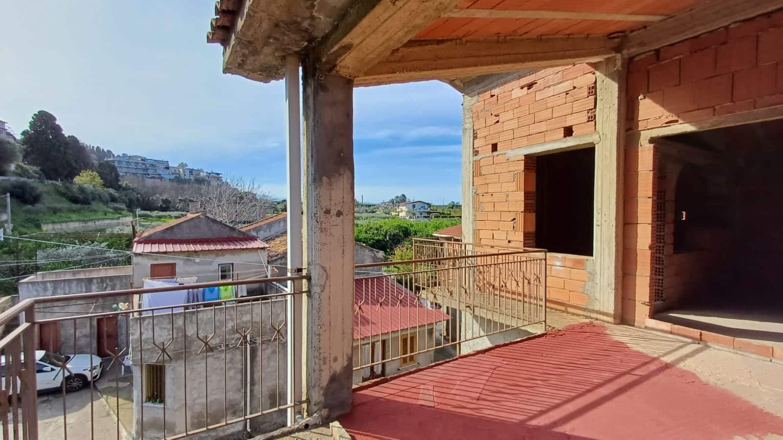 Balcone di un edificio in costruzione con vista su case e aree verdi in campagna, struttura in mattoni e balcone con ringhiera in metallo, ambiente in fase di finitura, NextCasa, immobili in vendita.
