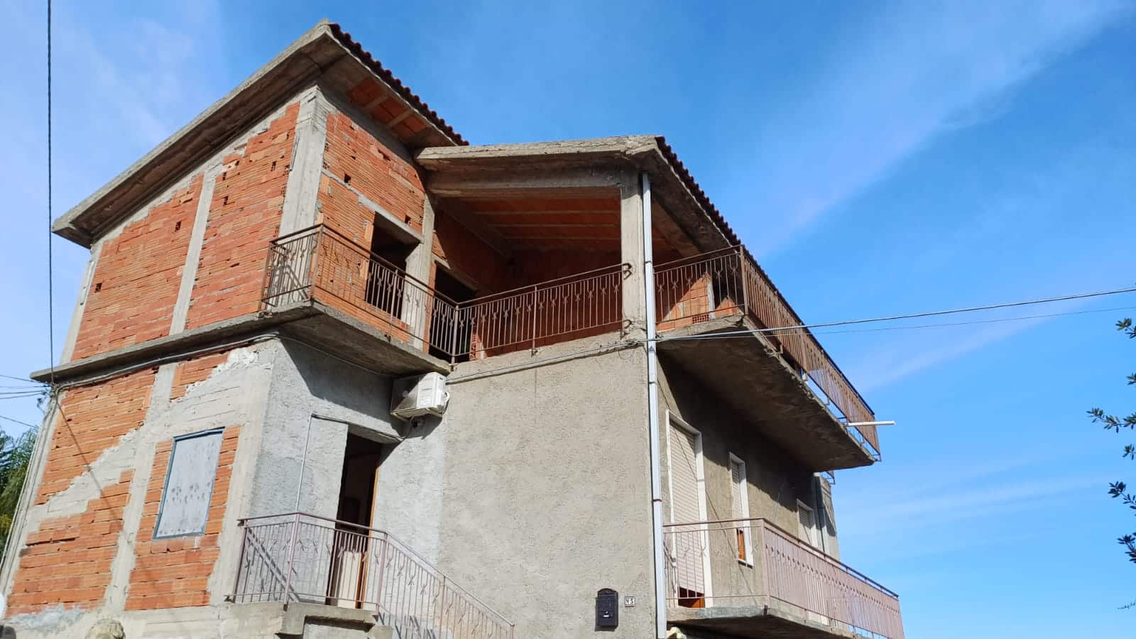 Villa in costruzione con balconi e struttura in mattoni, pronta per ristrutturazione, situata in zona tranquilla, ideale investimento immobiliare in Italia.