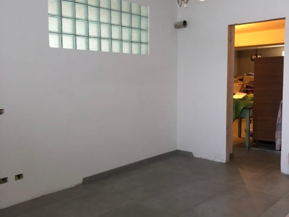 Finestra in vetrocemento su parete bianca, soffitto con lampadario vintage, pavimento in piastrelle grigie, interni di casa moderna, ambiente luminoso e spazioso, progetto immobiliare NextCasa.