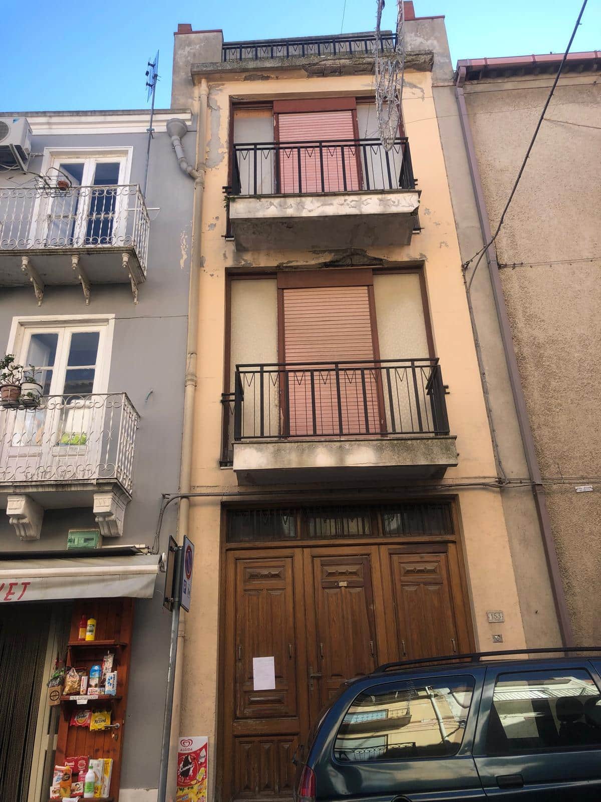 Vecchia facciata di edificio residenziale con balconi e portone in legno, in zona urbana, edificio da ristrutturare, esterno di casa con balconcini e ingresso principale in stile classico, NextCasa.