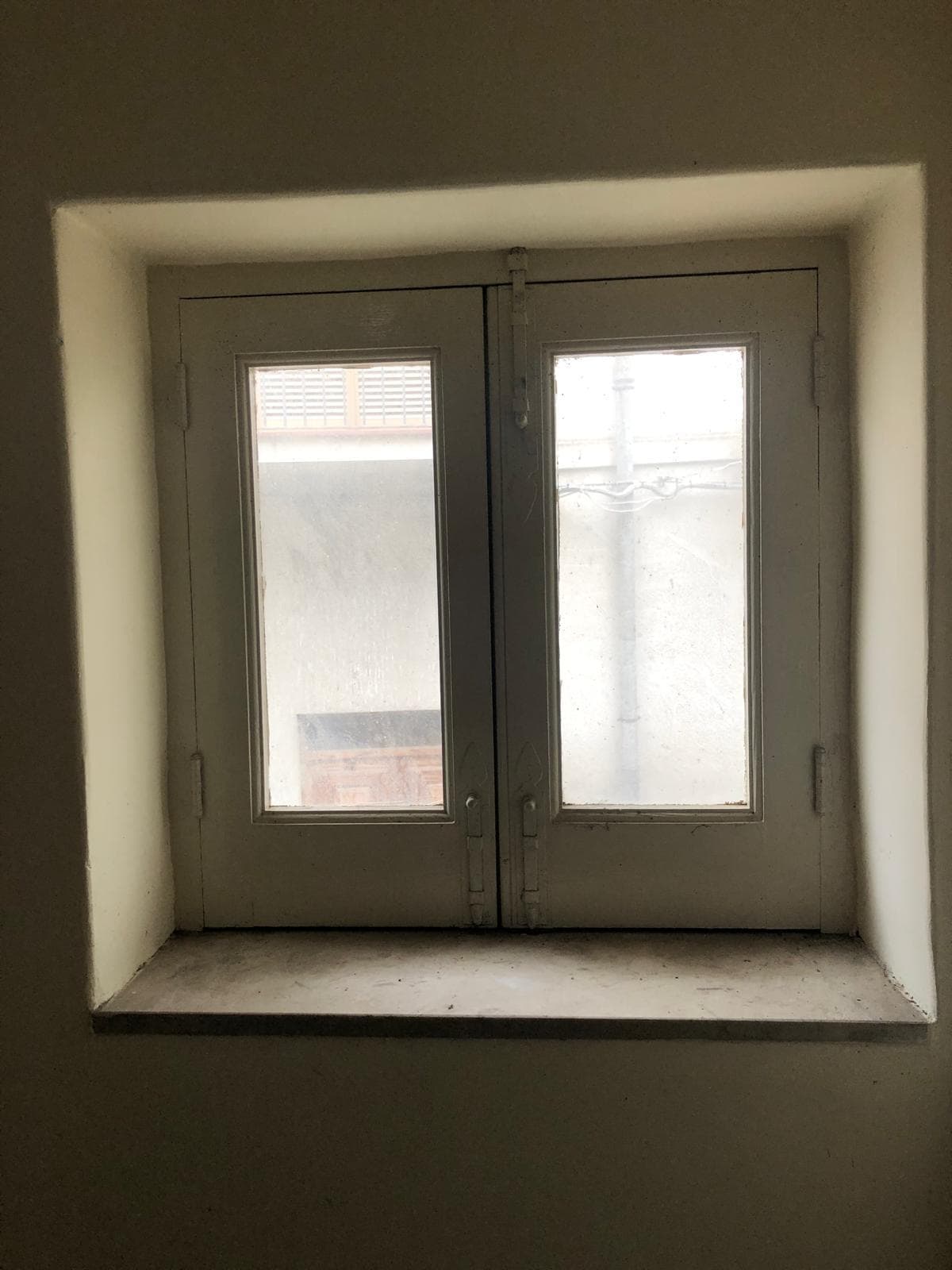 Veduta di una finestra in stile classico con doppia anta in PVC bianco, senza tende, in ambiente interno con pareti di colore chiaro, ideale per case e appartamenti in vendita o in affitto.