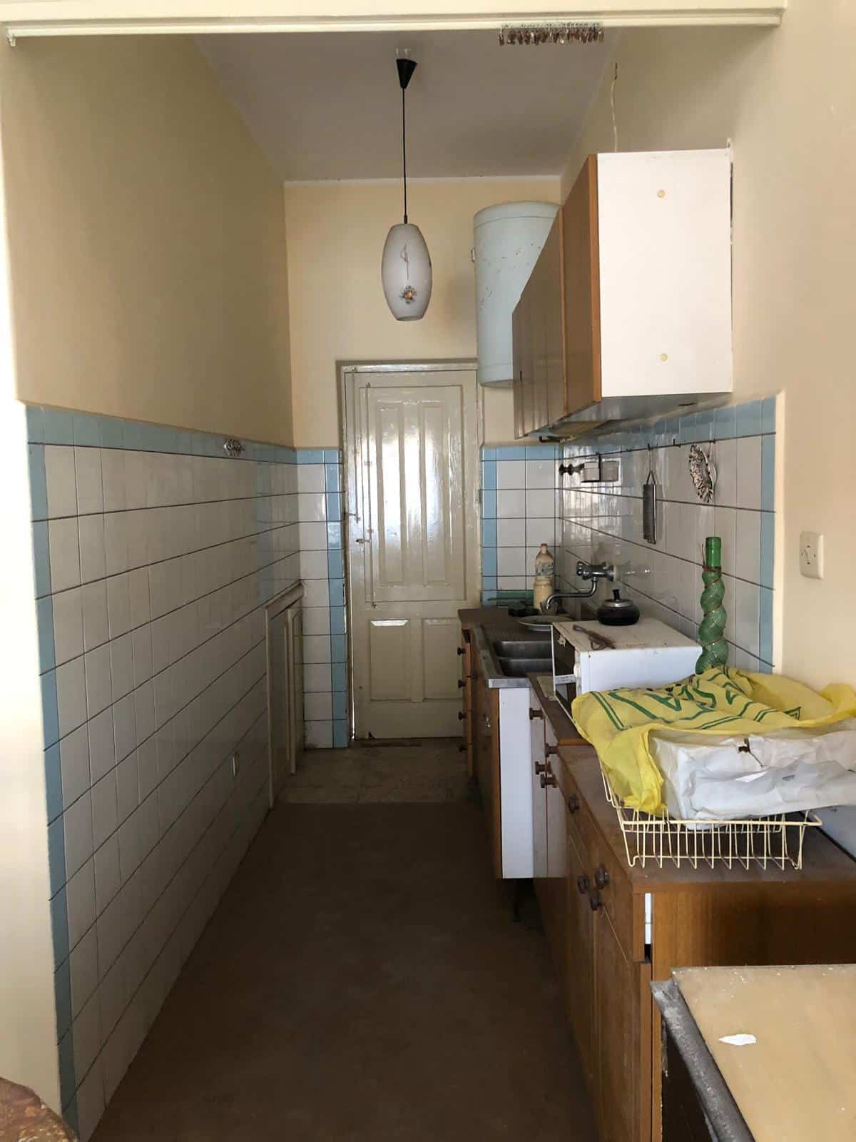 Rustico in vendita a NextCasa, piccola cucina con mobili di legno e utensili, pareti rivestite di piastrelle bianche e azzurre, soffitto sormontato da lampada a sospensione, porta in legno come ingresso.