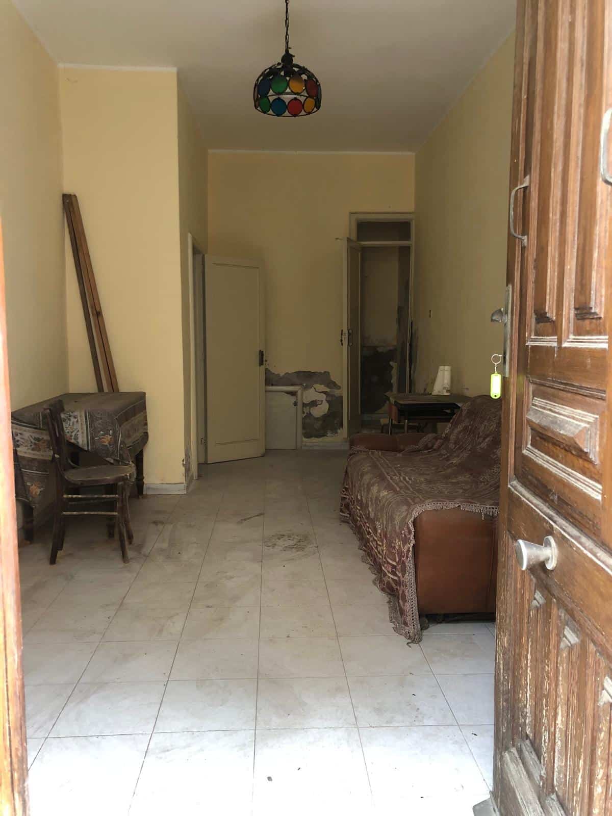 Riparazione casa, immobile da ristrutturare con mobili vintage e pavimento in gres porcellanato, soggiorno con divano e tavolo da pranzo, porte in legno e dettagli di arredamento.