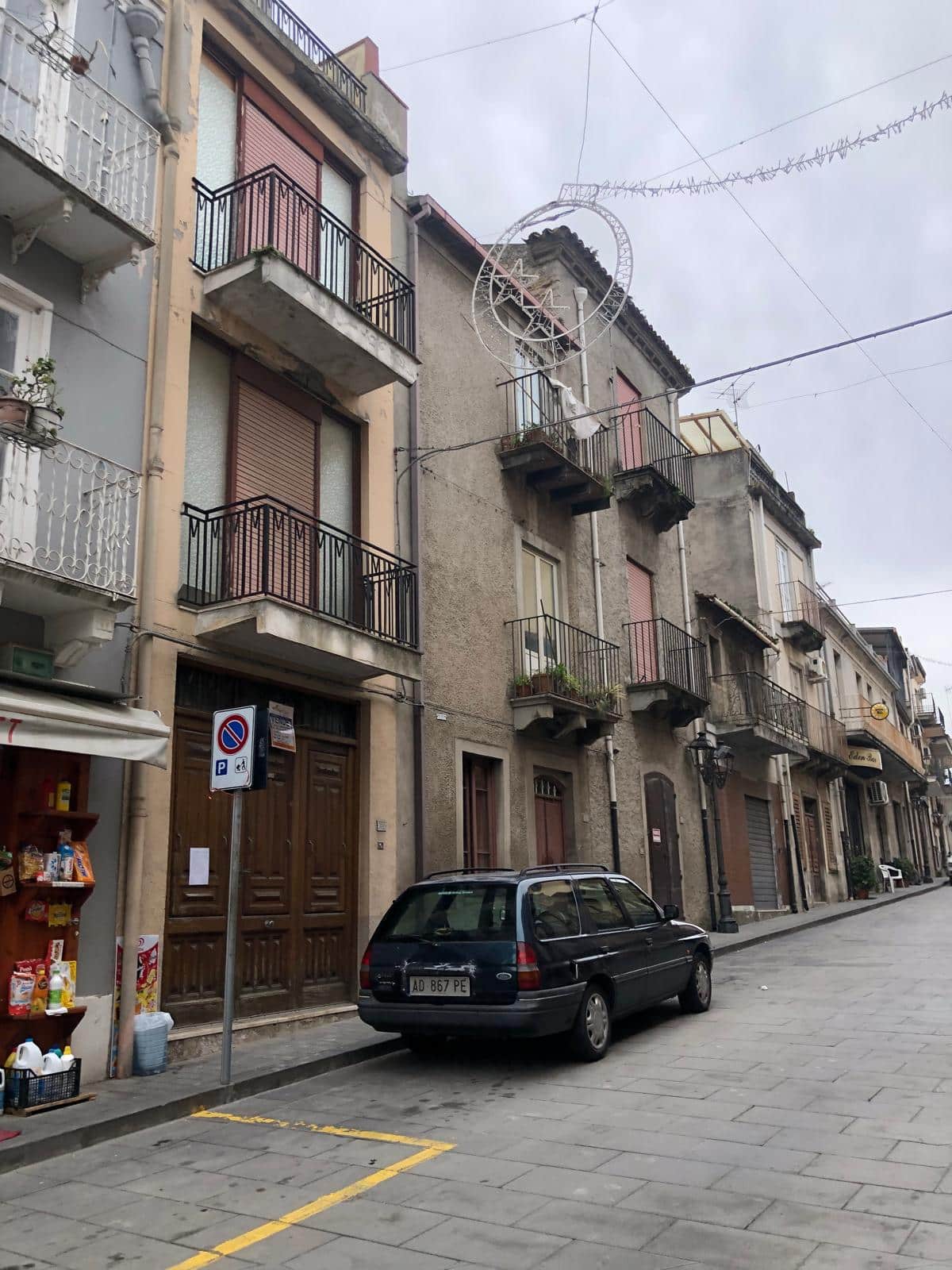 Balconi di palazzi storici con installazioni decorative, in zona urbana con auto parcheggiate e negozi di vicinato, rappresentano l'architettura residenziale e commerciale di città italiane.