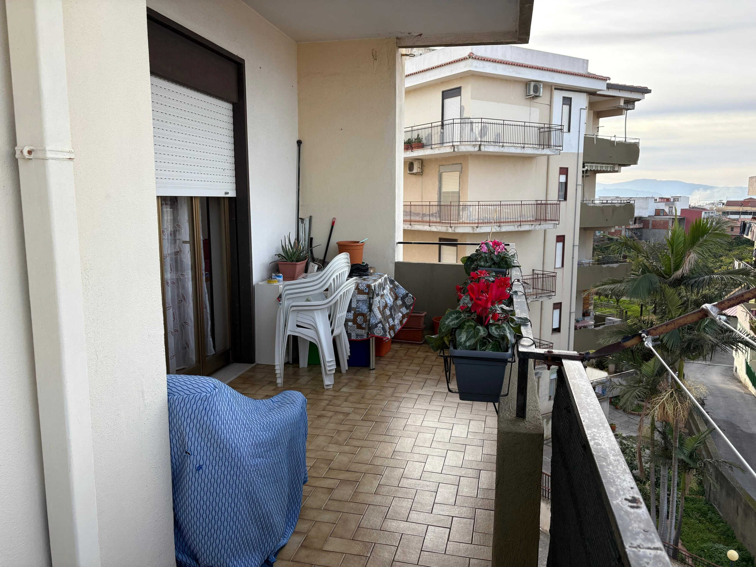 Balcone di un appartamento con piante e mobili da esterno, vista su edifici residenziali e landscape urbano, ideale per relax e convivialità, in zona abitativa di città.
