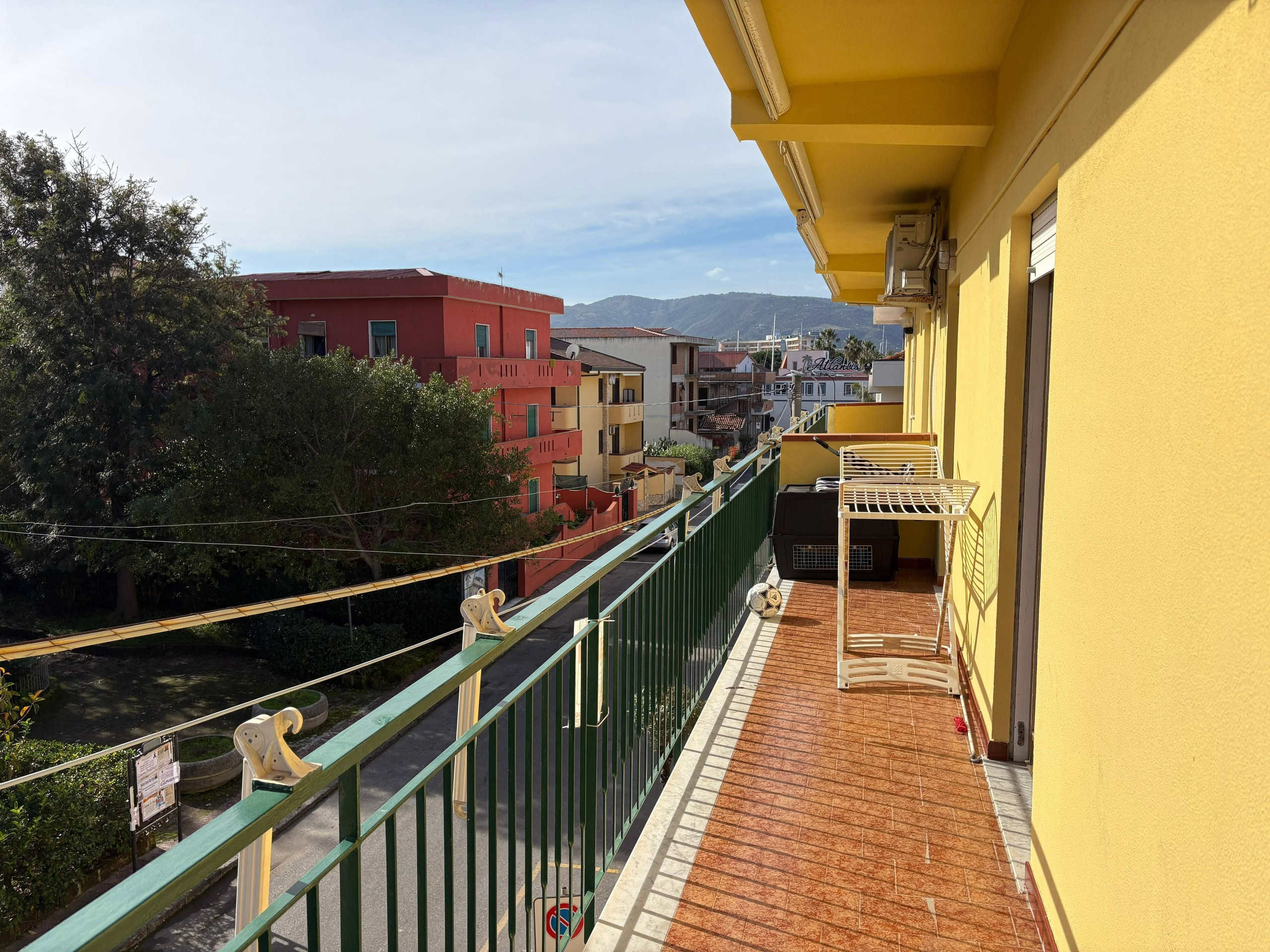Balcone di un appartamento con vista sulla città e le montagne, pavimentato in gres porcellanato color terracotta, arredato con stendibiancheria, aria condizionata e vista panoramica.