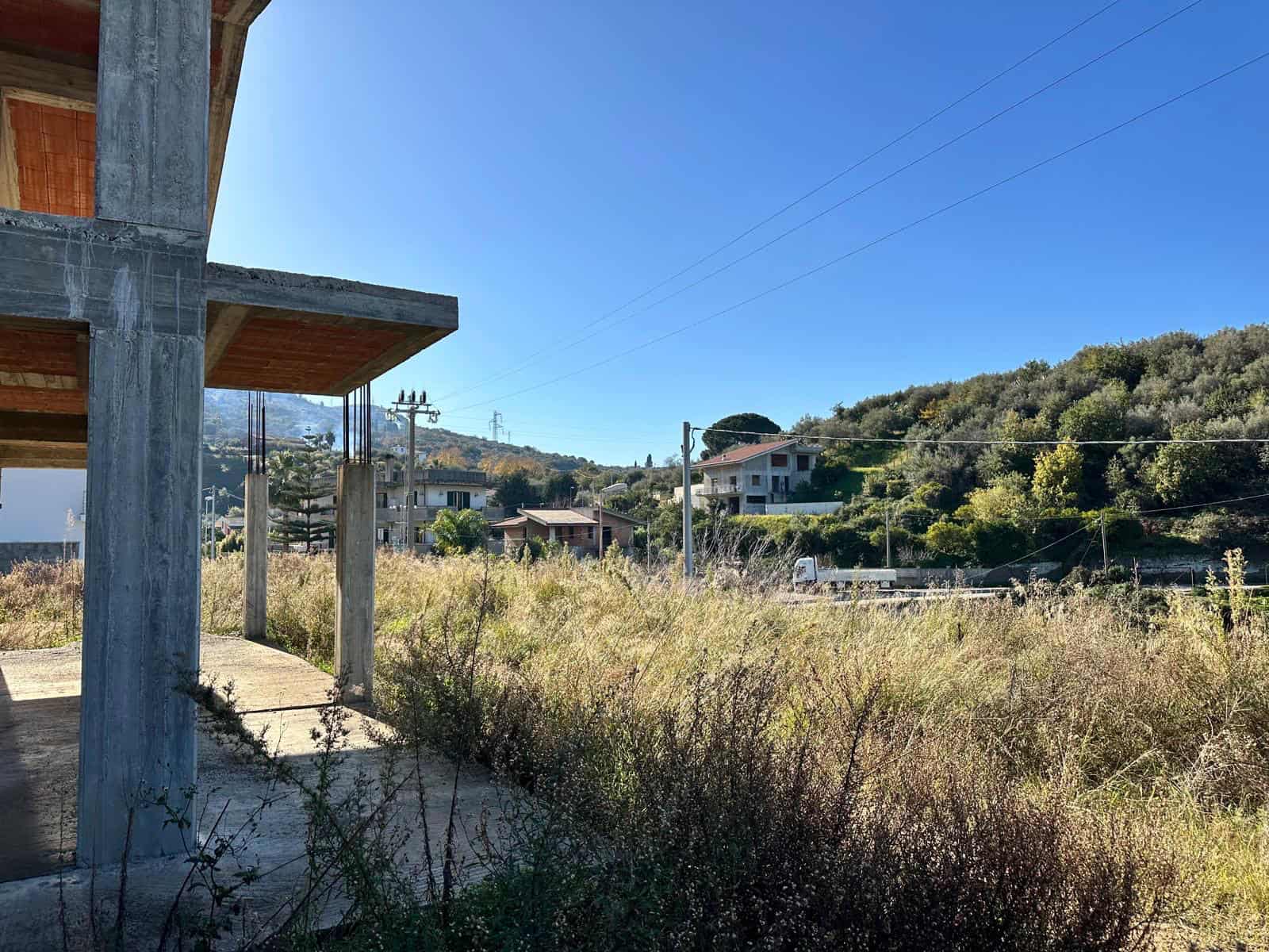 Cantiere edilizio su un terreno naturale con vista su case e colline, in fase di costruzione di immobili residenziali, con strutture in cemento e panorama di montagna in background.