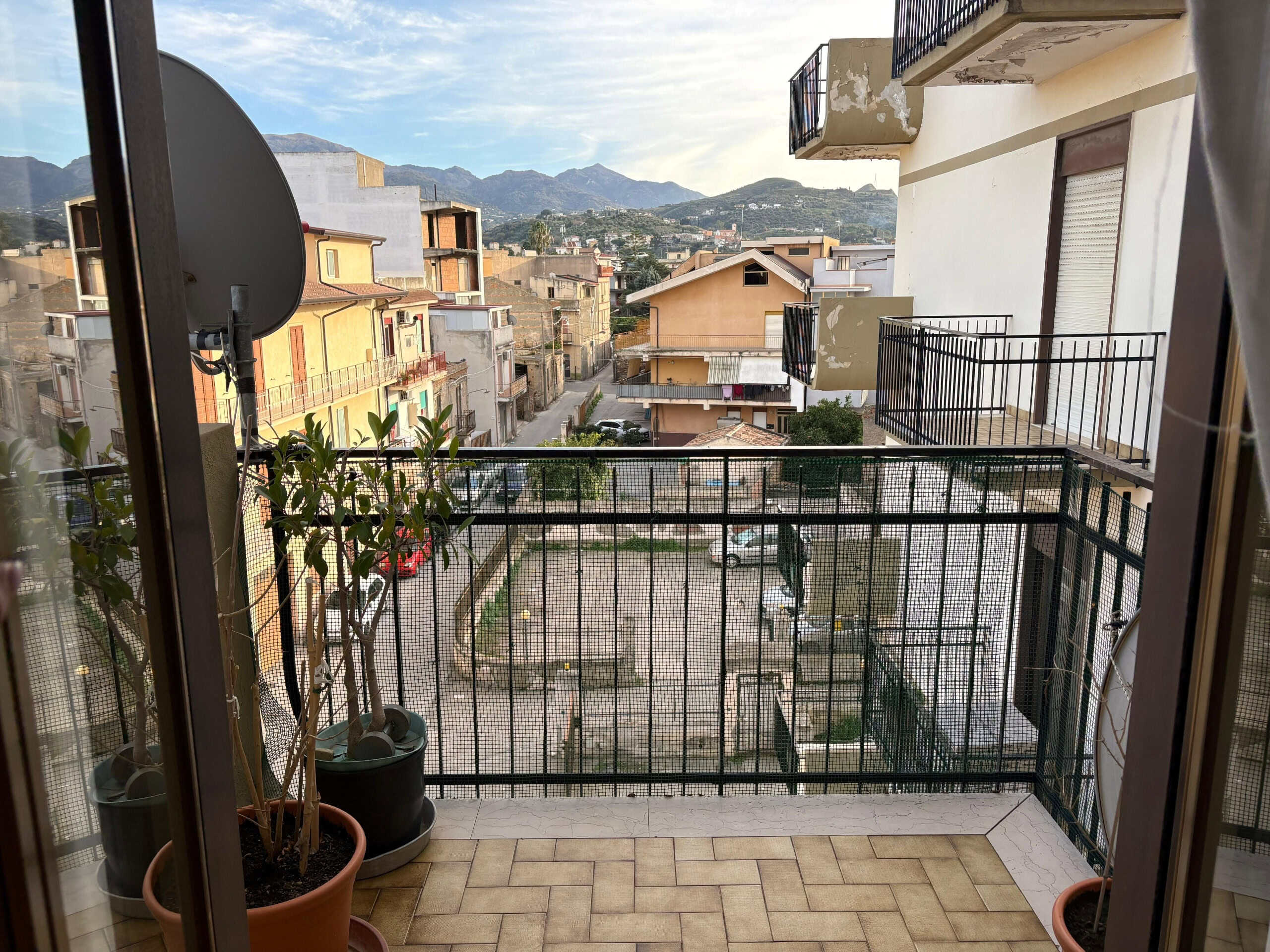Balcone con vista su quartiere residenziale e montagne, con piante in vaso, in un appartamento in vendita o affitto a NextCasa.