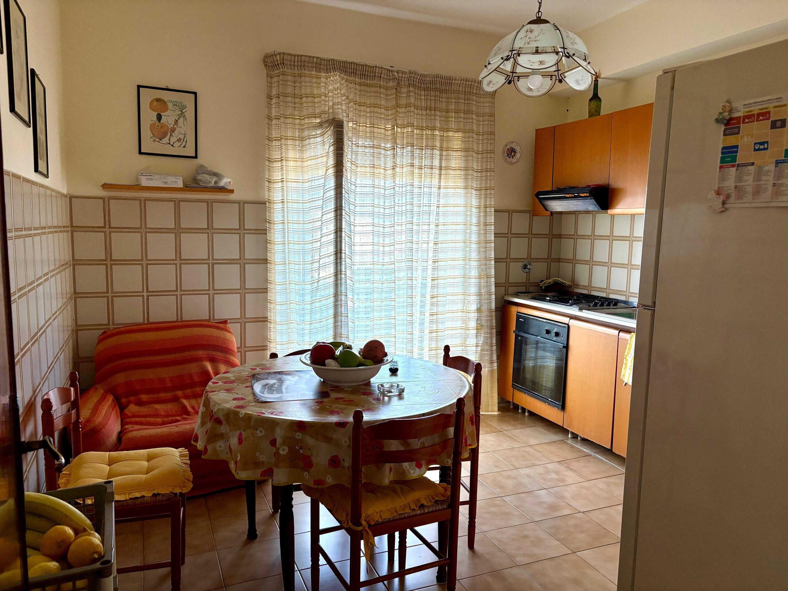 UFFICIO:[NextCasa, cucina abitabile con tavolo da pranzo, sedie e divano, in stile semplice e funzionale, con accessori e decorazioni in ambiente luminoso e accogliente, pareti rivestite in piastrelle color beige e accesso a balcone o fonte di luce naturale].