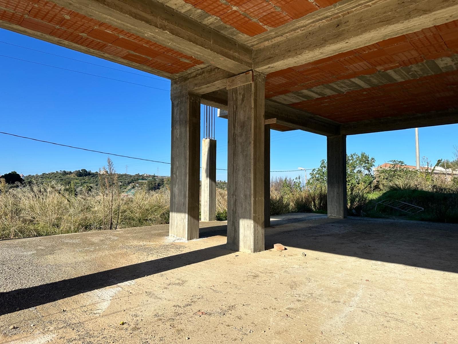 FOTO-1: Struttura in cemento di una casa in costruzione in campagna, con soffitto in calcestruzzo e colonne a vista, sotto un cielo sereno.