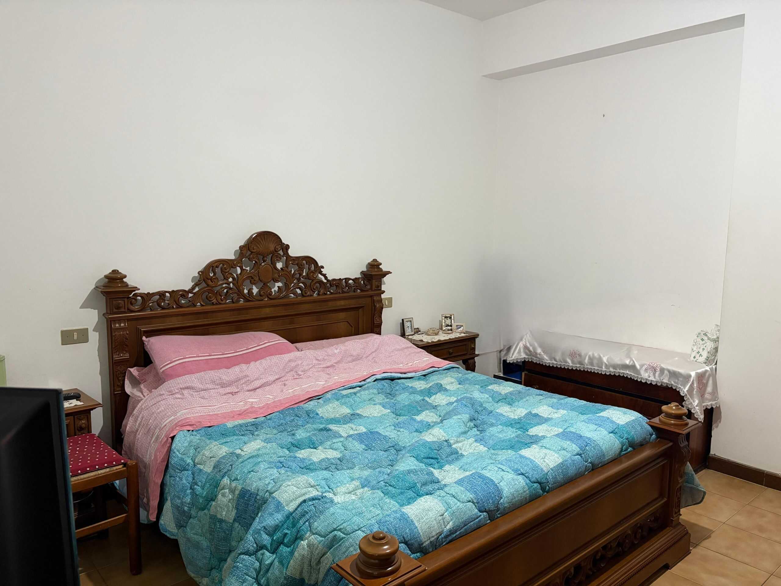 Letto matrimoniale in stile classico con testiera in legno intagliato, camera da letto spaziosa e arredata con mobili tradizionali, ideale per case in vendita o affitto a NextCasa.