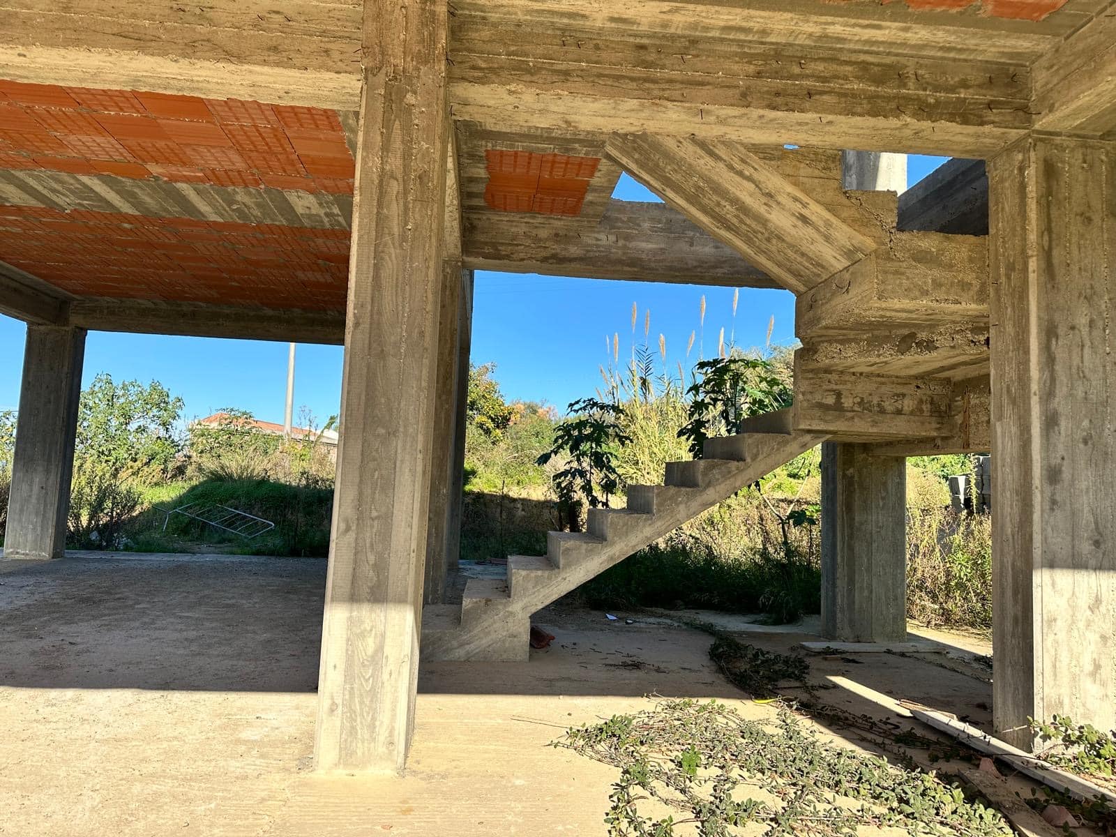 Architettura in costruzione con struttura in cemento e scala infissa, ambiente esterno con natura e cielo azzurro, progetto edilizio NextCasa, opportunità di investimento immobiliare.