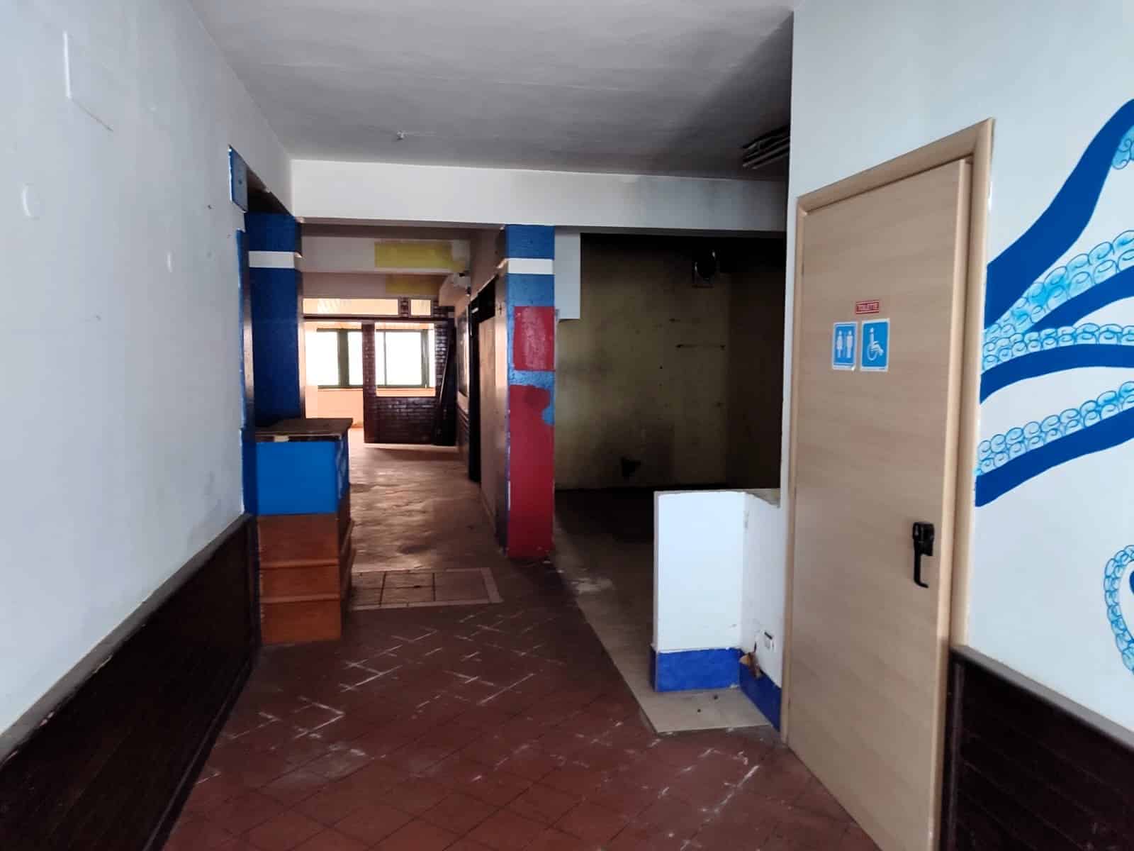 Immagine di un corridoio interno di un immobile con pareti decorati, pavimento in piastrelle e accesso a servizi igienici e area comune, ideale per promuovere spazi residenziali e commerciali su NextCasa.