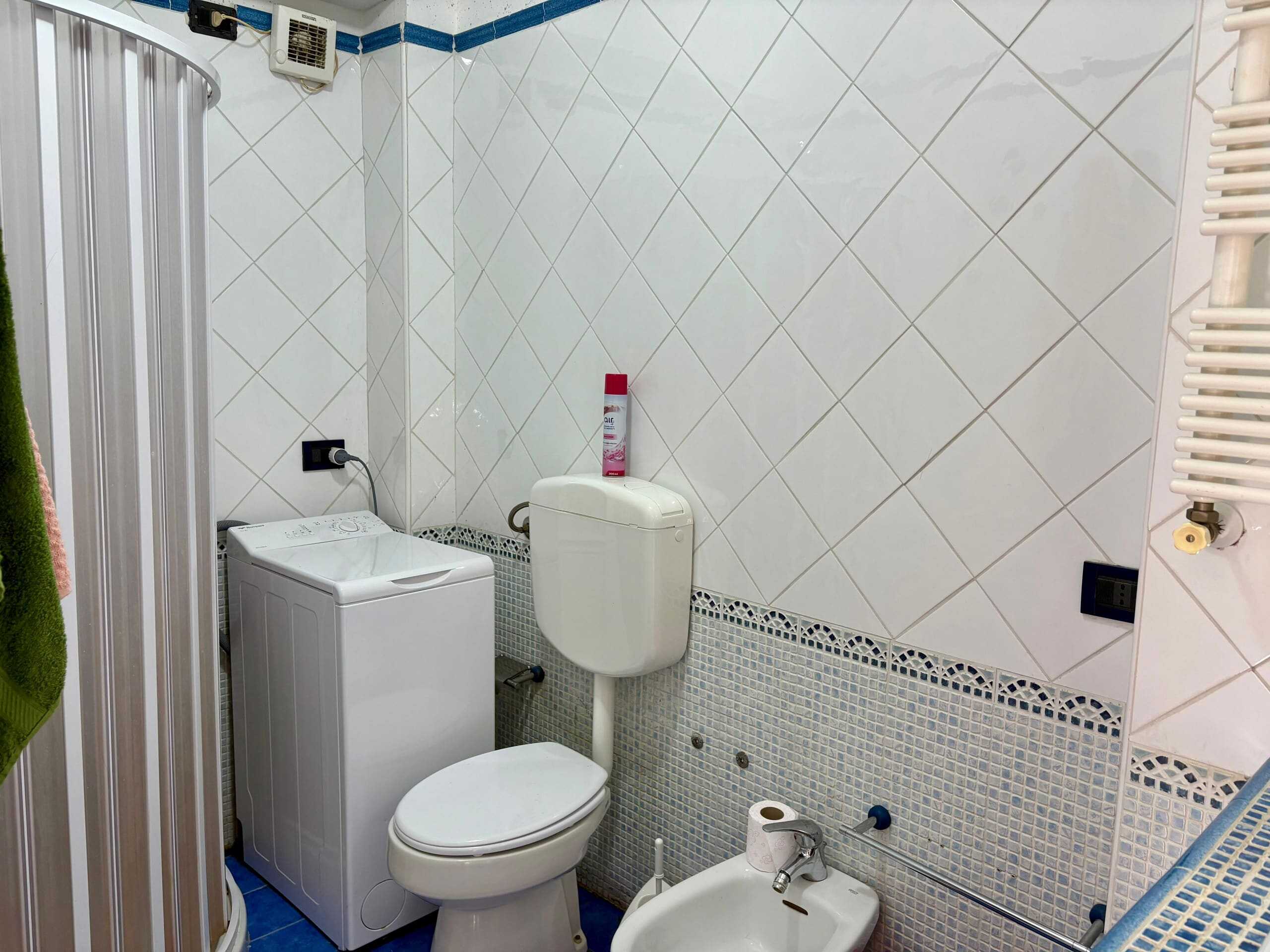 Lavatrice, bagno con sanitari e pareti rivestite in piastrelle bianche, dettagli di arredo bagno in Italia, comfort e funzionalità per la casa.