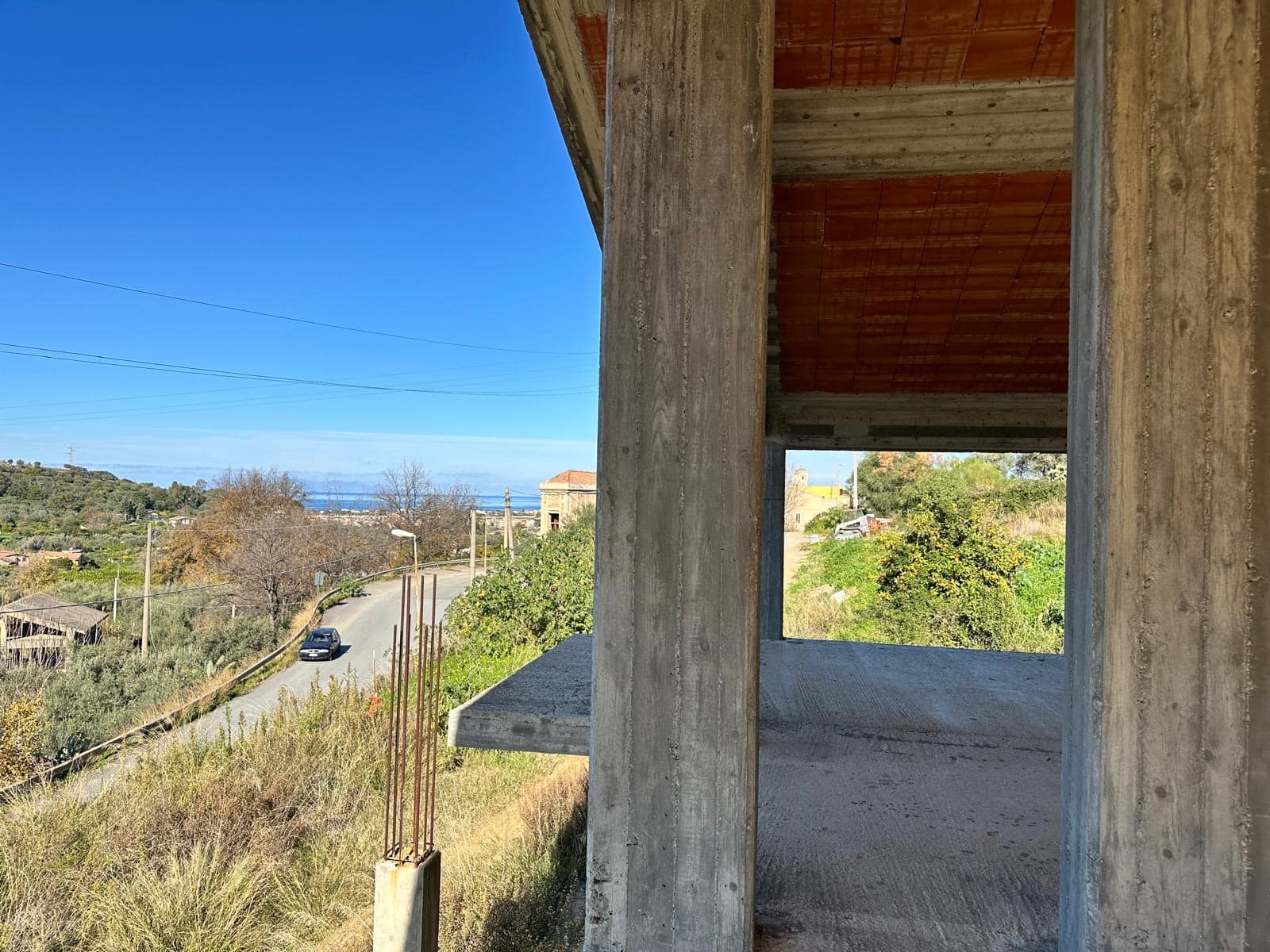 Vista panoramica di un edificio in costruzione con un paesaggio naturale, strade e cielo blu sullo sfondo, ideale per immagini di immobili in fase di sviluppo o progettazione edilizia.
