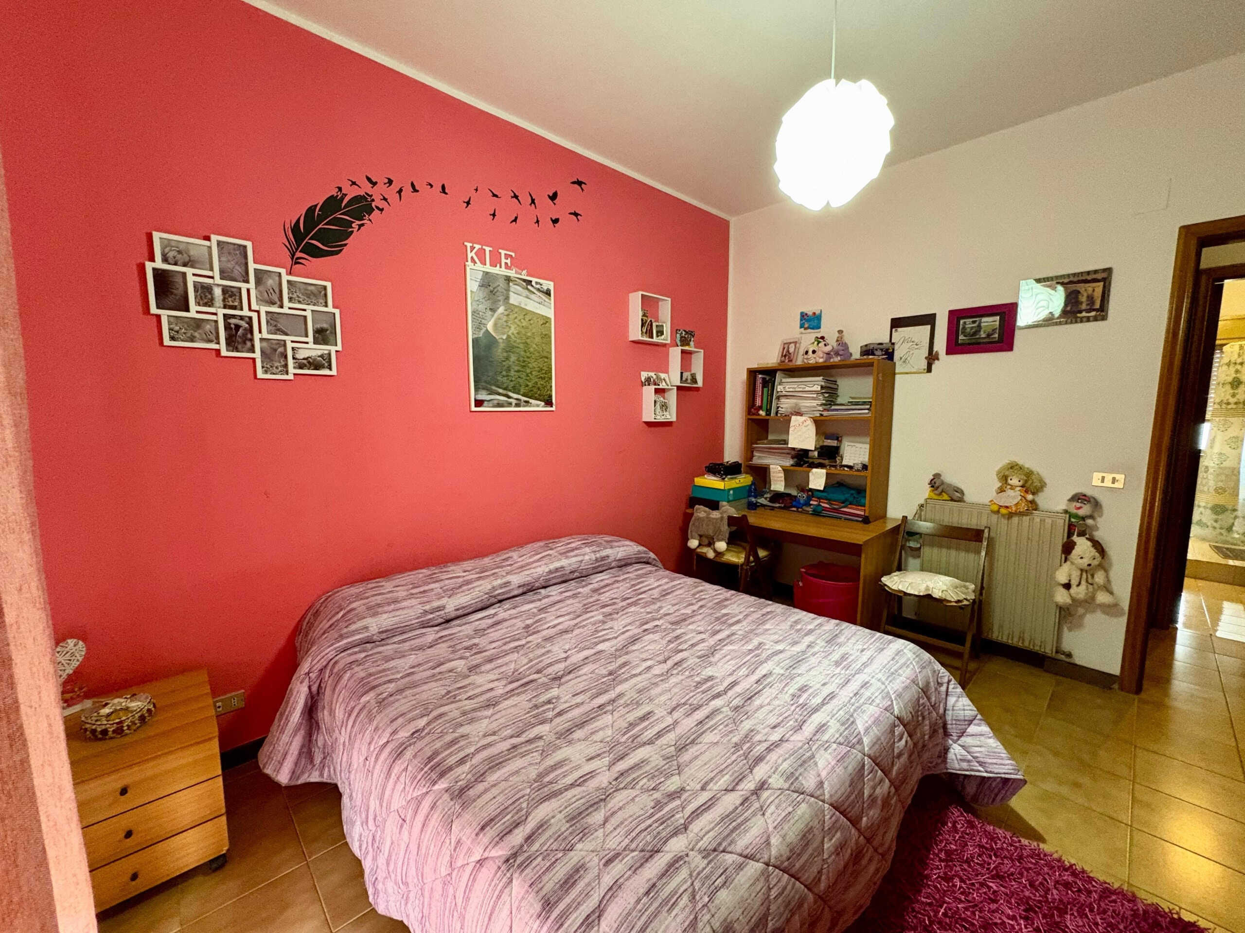 Letto matrimoniale con parete rossa decorata con foto e quadri, ambiente accogliente e personalizzato, ideale per una camera da letto casalinga.