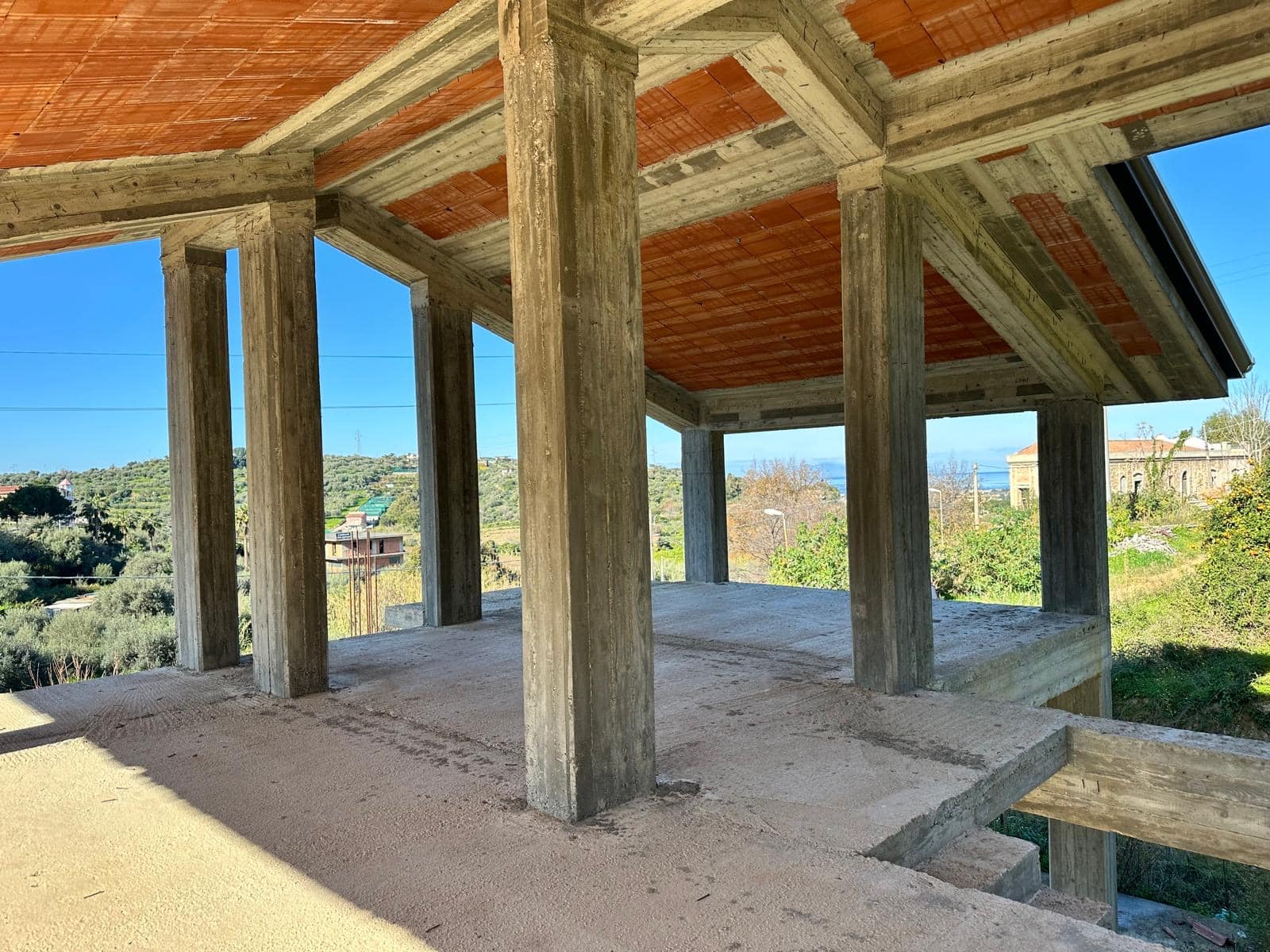 Struttura in cemento e legno di una casa incompiuta in costruzione, con vista panoramica sul territorio circostante, in un contesto residenziale e naturale, ancora in fase di sviluppo.