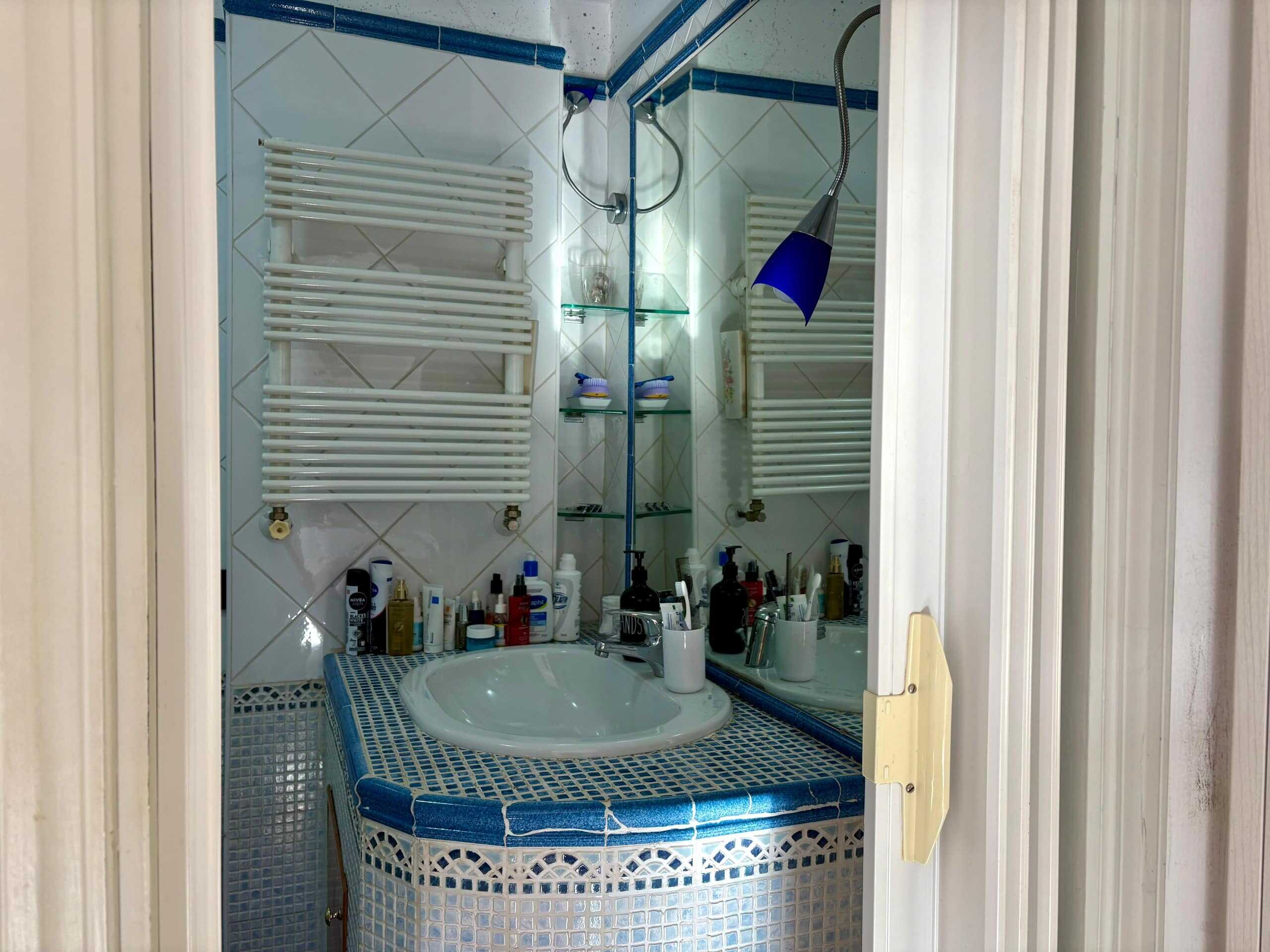 Lavandino con mobili bagno stretti e specchio con scaffale in vetro, asciugamani riscaldati e prodotti per la cura della persona, in un bagno di lusso vicino a NextCasa.