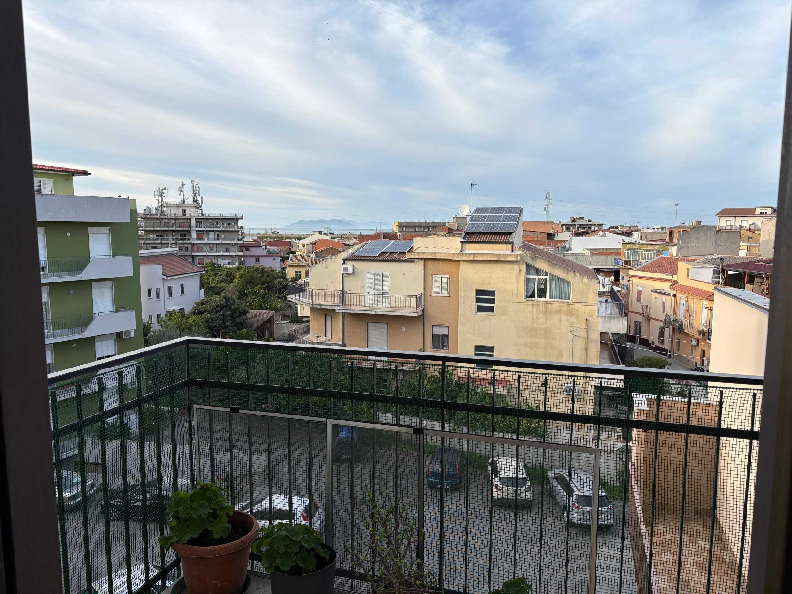 Balcone con vista su edifici residenziali e tetti, con pannelli solari, in una città italiana soleggiata e moderna, atmosfera tranquilla e urbanistica contemporanea.